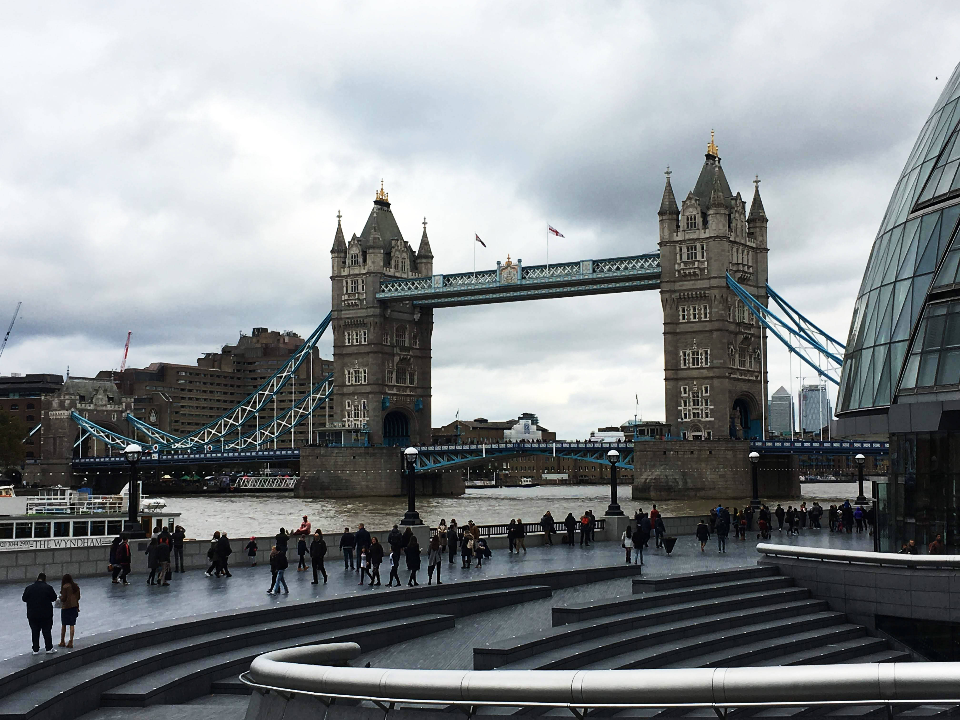 bridge 桌布 壁紙 — 倫敦塔橋在陰天之下雄偉地橫跨泰晤士河，行人沿著現代化的河濱步道漫步。