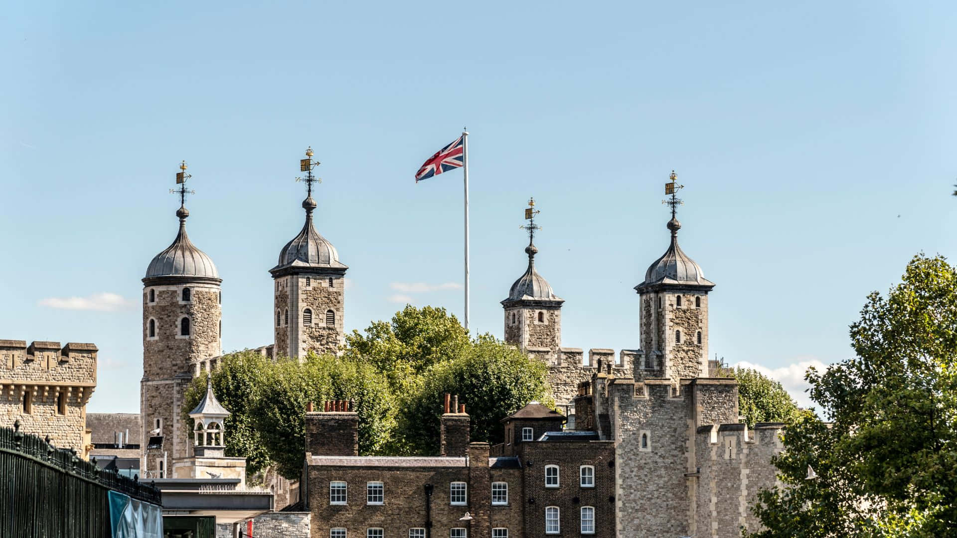 UK 桌布 壁紙 — 倫敦塔的石塔在清澈的藍天下聳立，一根旗桿上飄揚著英國國旗。