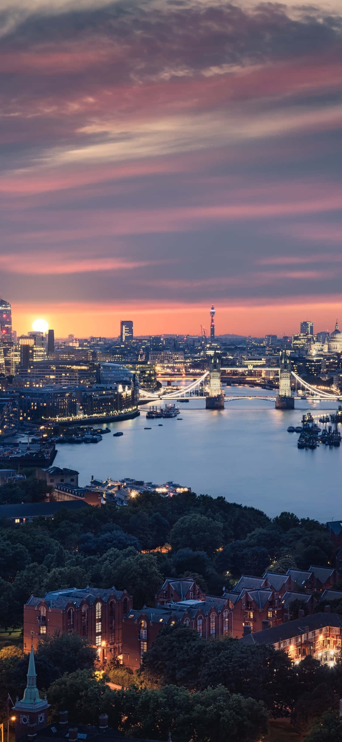 London iPhone 桌布 壁紙 — 倫敦天際線在黃昏時分，塔橋在泰晤士河上空鮮豔的粉紅色和橙色天空映襯下亮起。