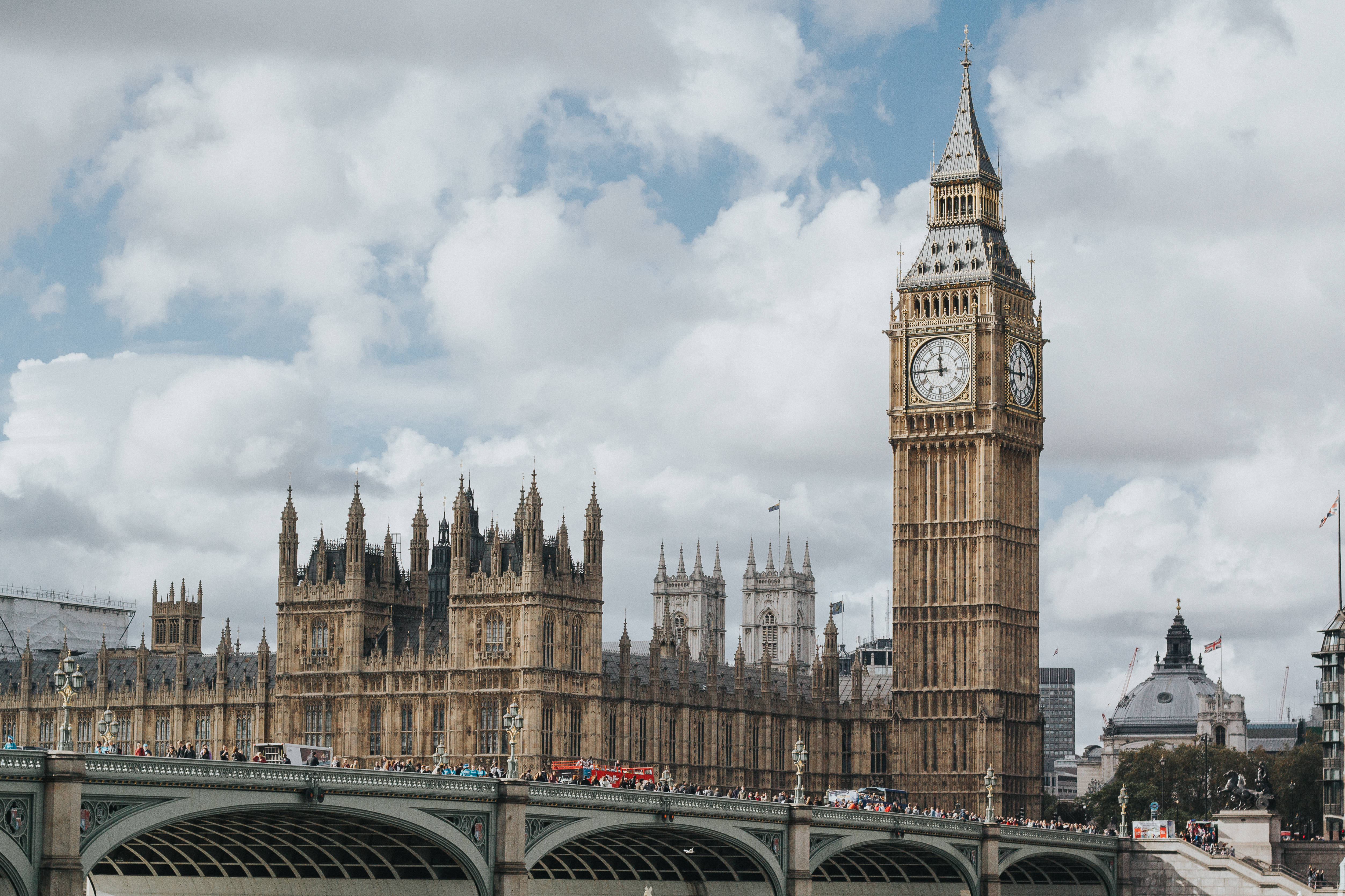 England 桌布 壁紙 — 倫敦標誌性的伊莉莎白塔和國會大廈在部分多雲的天空下巍然聳立，下方橋樑上行人與車輛熙熙攘攘。