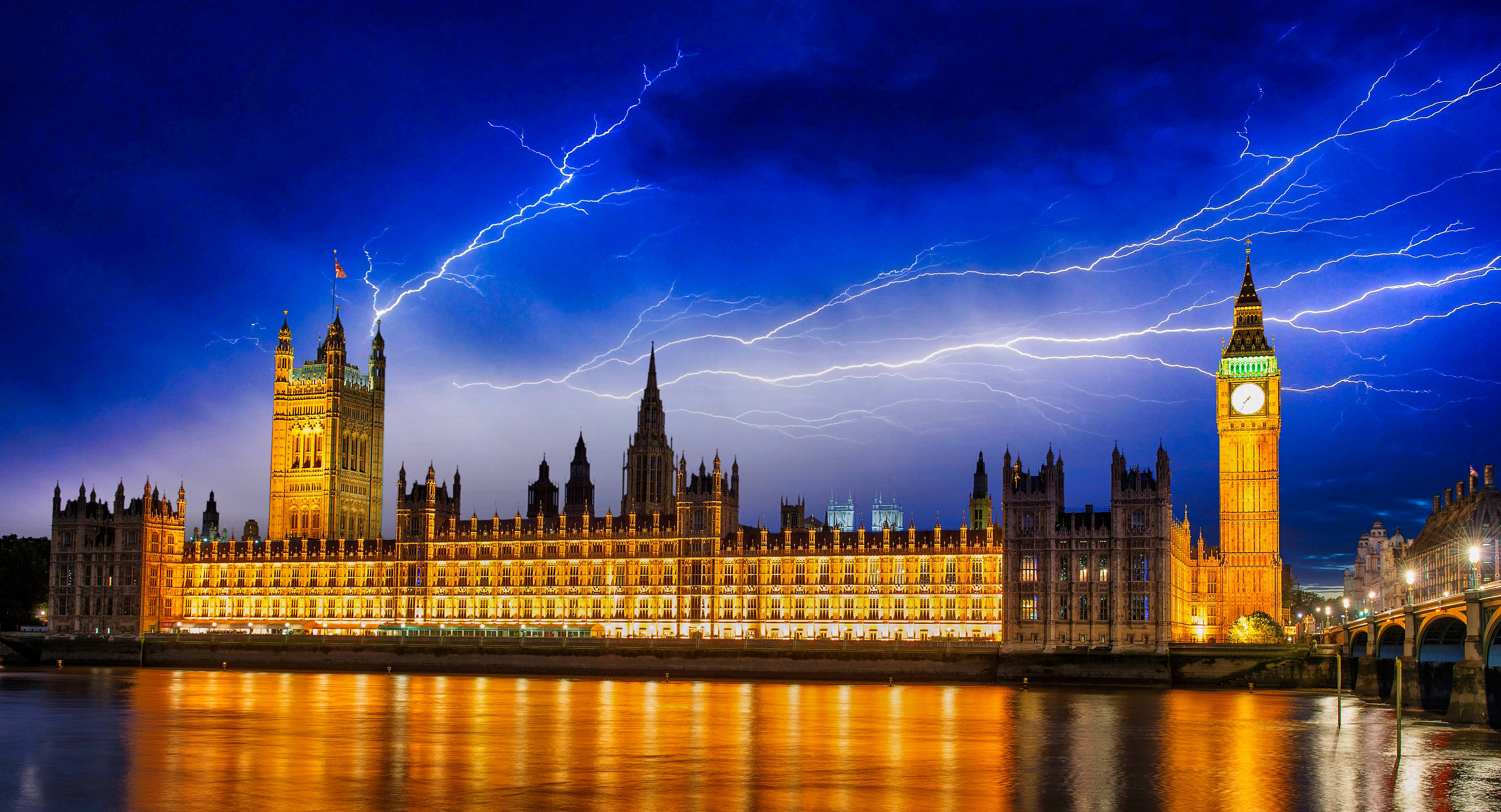 United Kingdom 桌布 壁紙 — 倫敦標誌性的國會大廈和大本鐘在佈滿閃電的戲劇性天空下溫暖地發光。