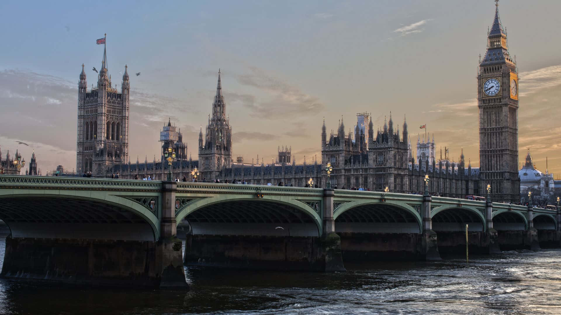 UK 桌布 壁紙 — 倫敦標誌性的大笨鐘和國會大廈在日落時分溫暖地發光，泰晤士河在威斯敏斯特橋下流淌。