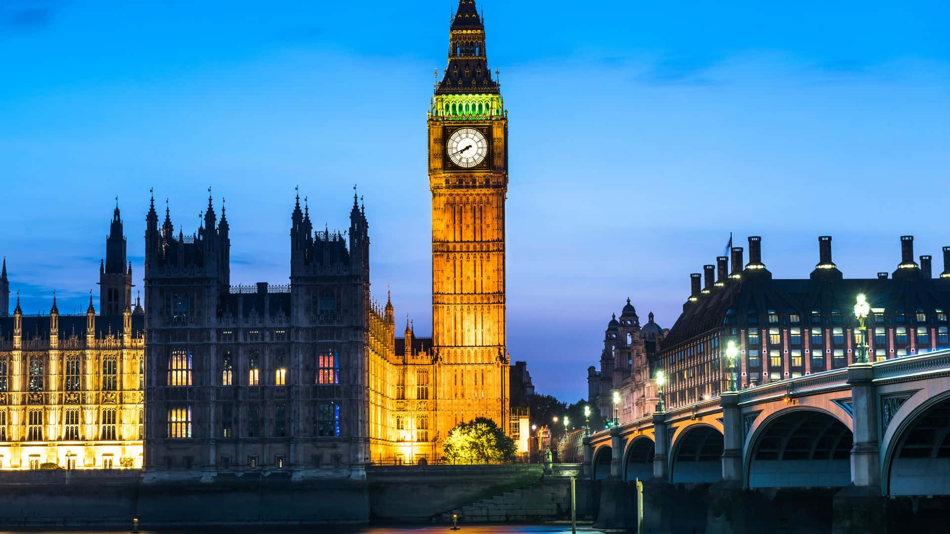 UK 桌布 壁紙 — 倫敦標誌性的大笨鐘和國會大廈在黃昏時亮起溫暖的燈光，倒映在泰晤士河上。