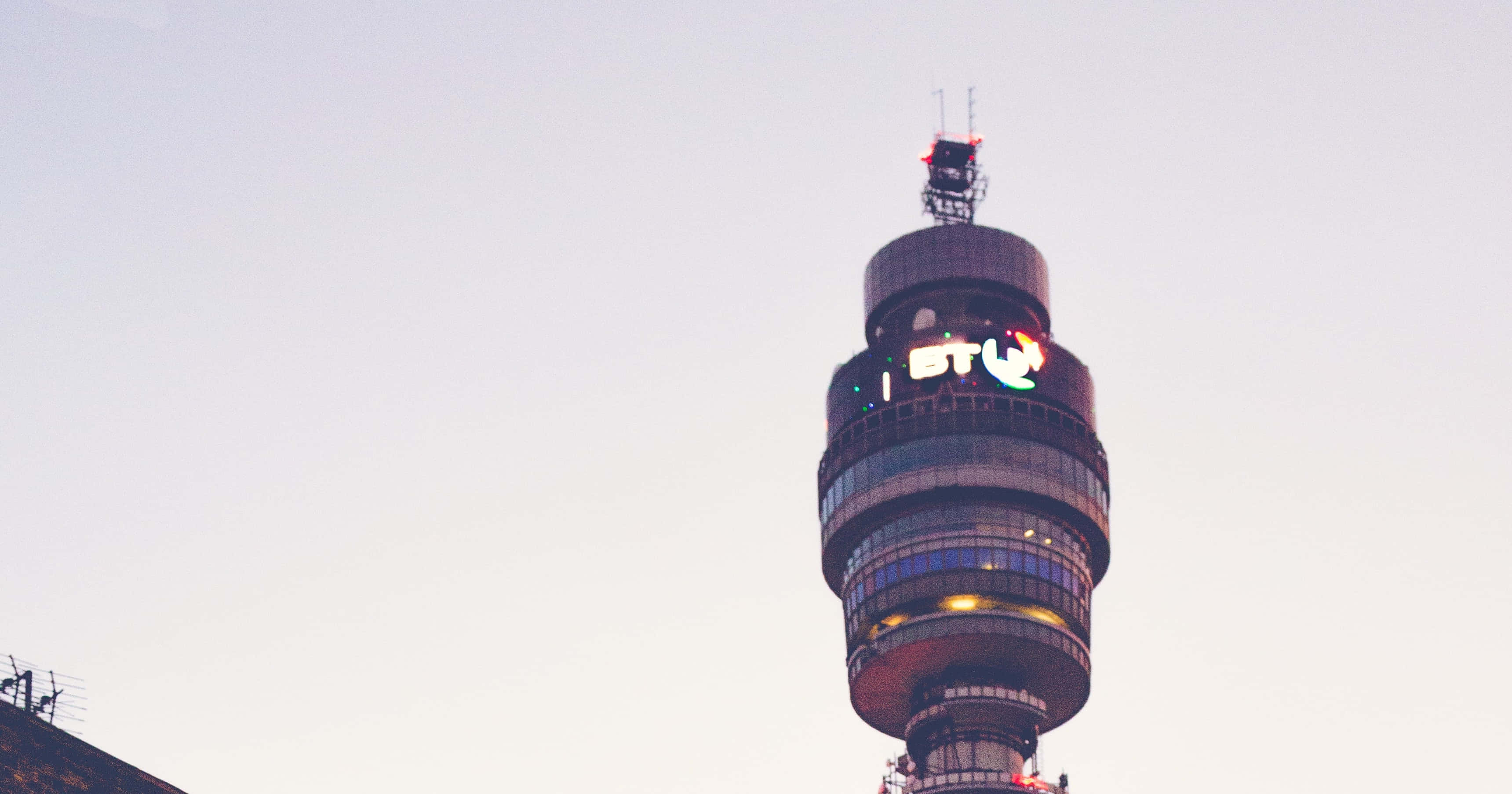 tower 桌布 壁紙 — 倫敦的BT塔在蒼白的天空下高聳入雲，其標誌性的發光標誌在黃昏時閃耀。