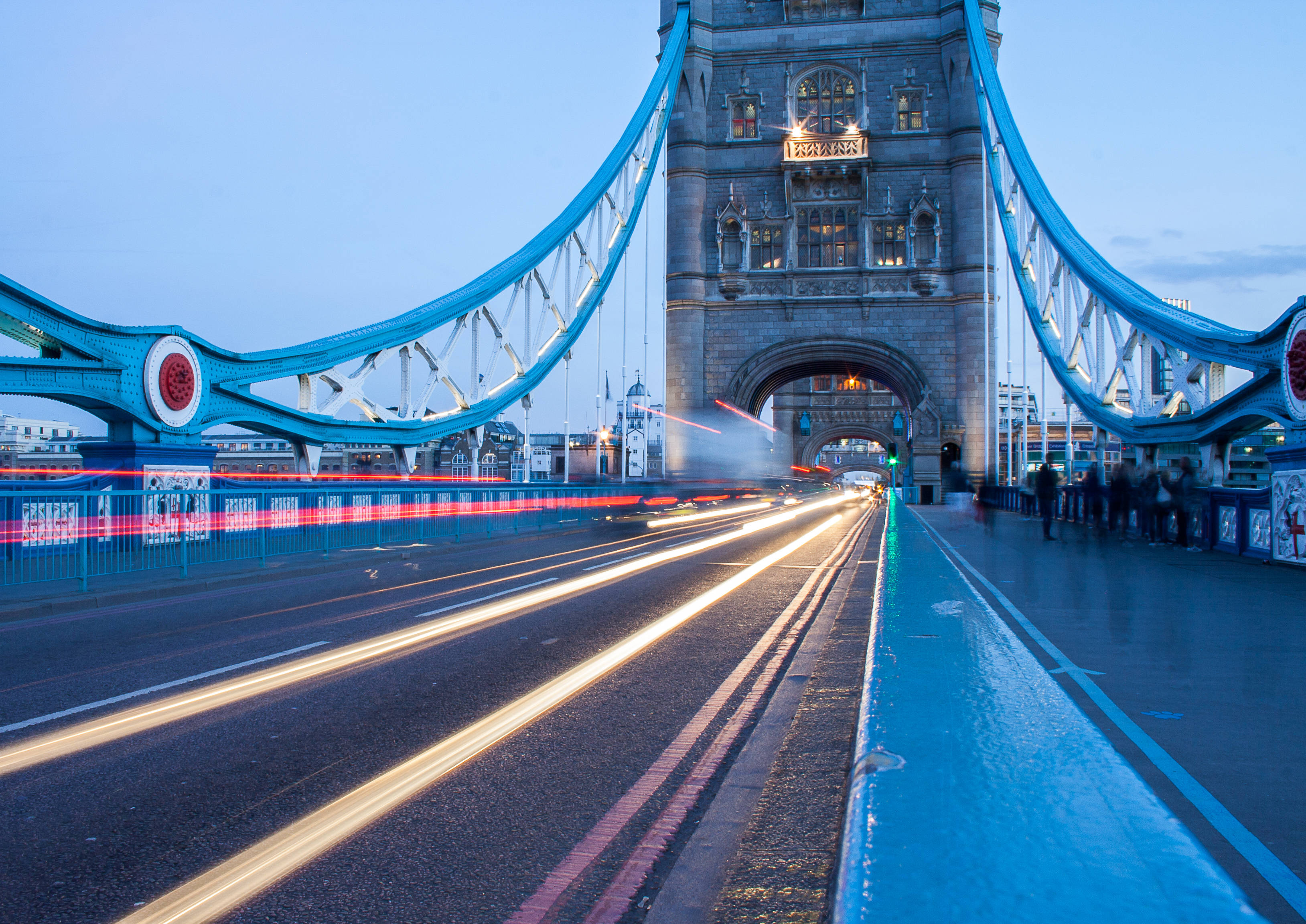 bridge 桌布 壁紙 — 倫敦的塔橋在暮色中閃耀，汽車燈光的條紋在其標誌性的藍色懸索結構上模糊掠過。
