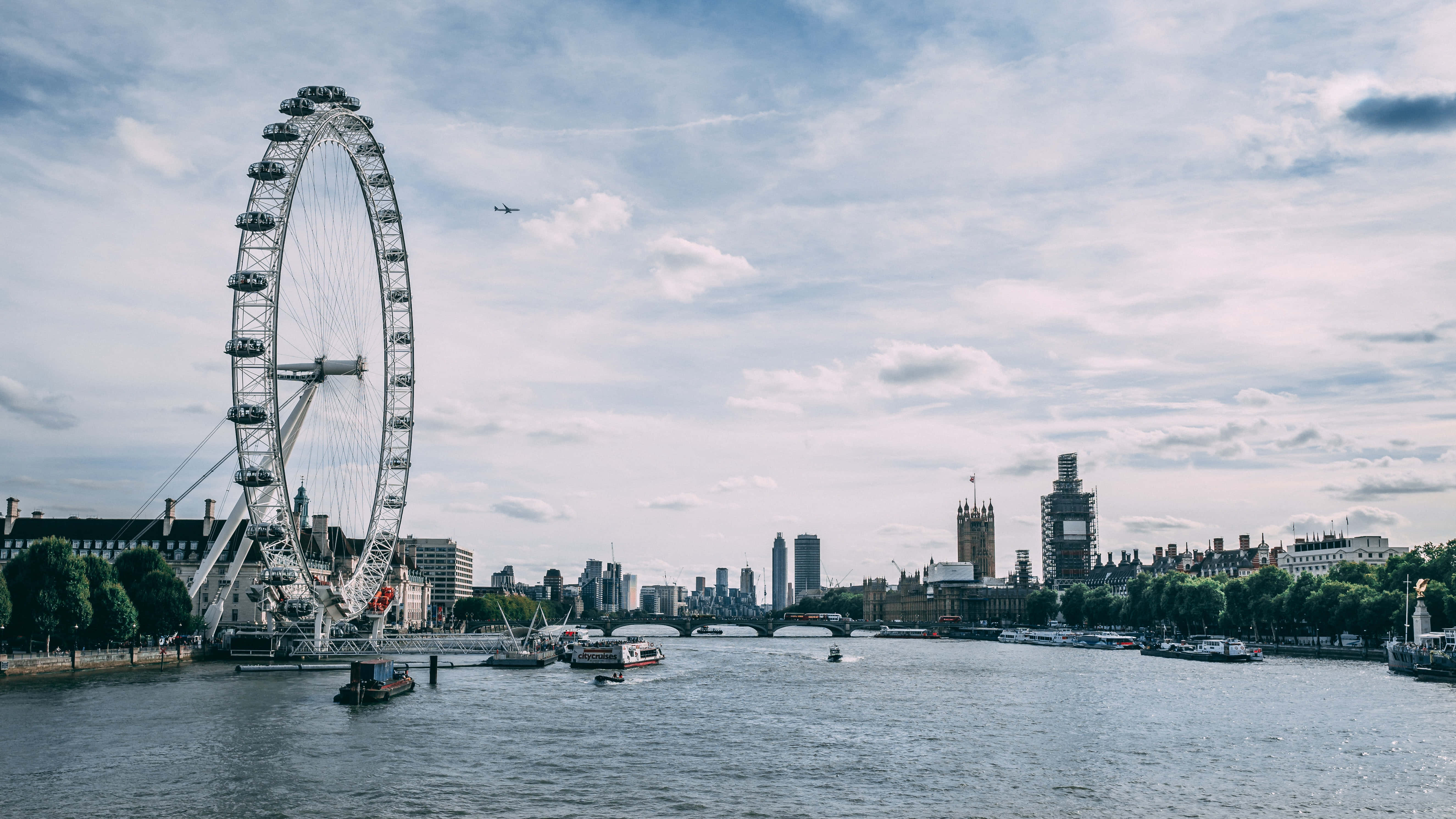England 桌布 壁紙 — 倫敦眼主導泰晤士河，船隻在其巨大結構下滑行，背景是部分多雲的天空。