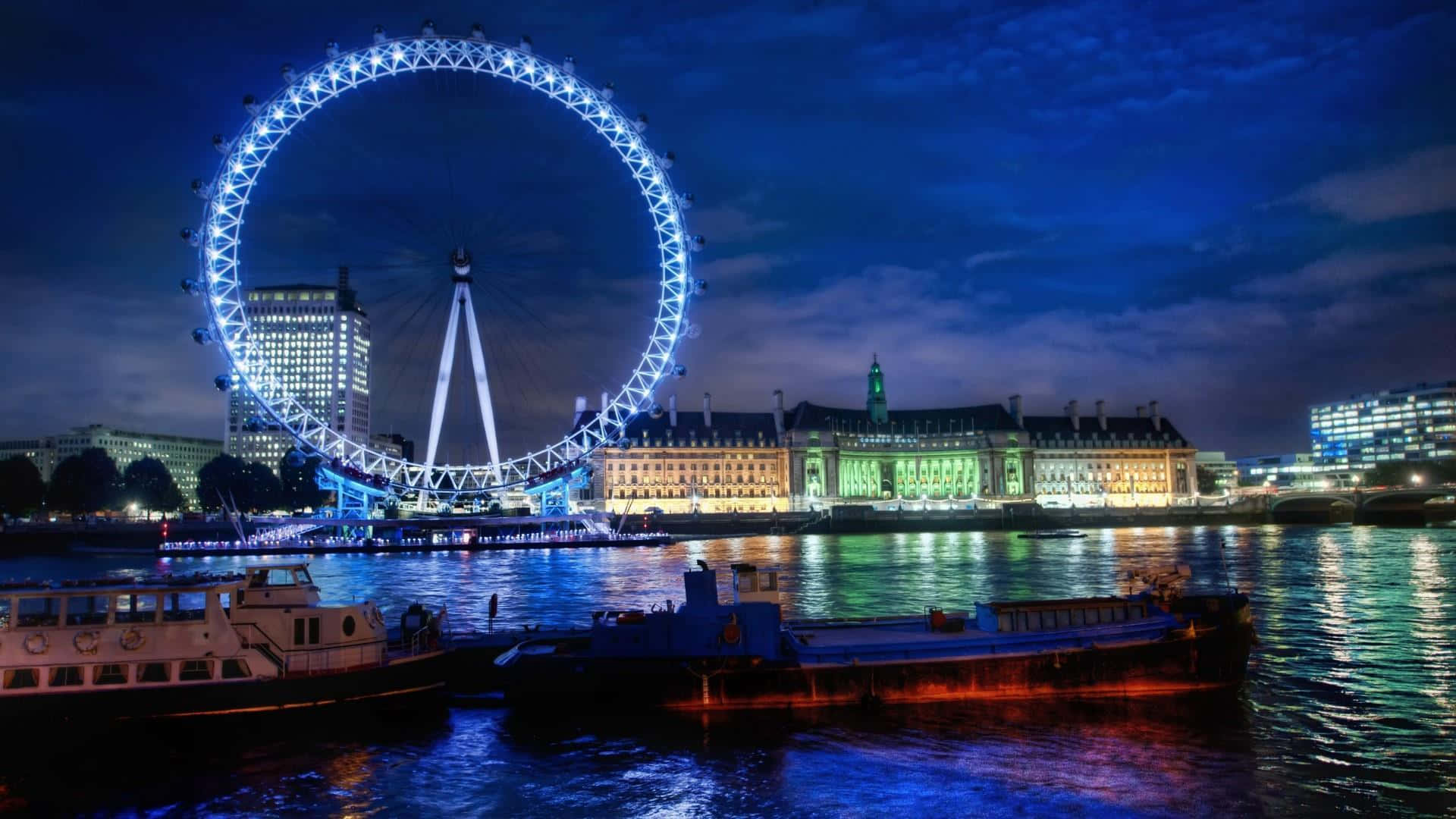 England 桌布 壁紙 — 倫敦眼在暮色中發出藍光，燈光倒映在泰晤士河上，下方停泊著船隻。