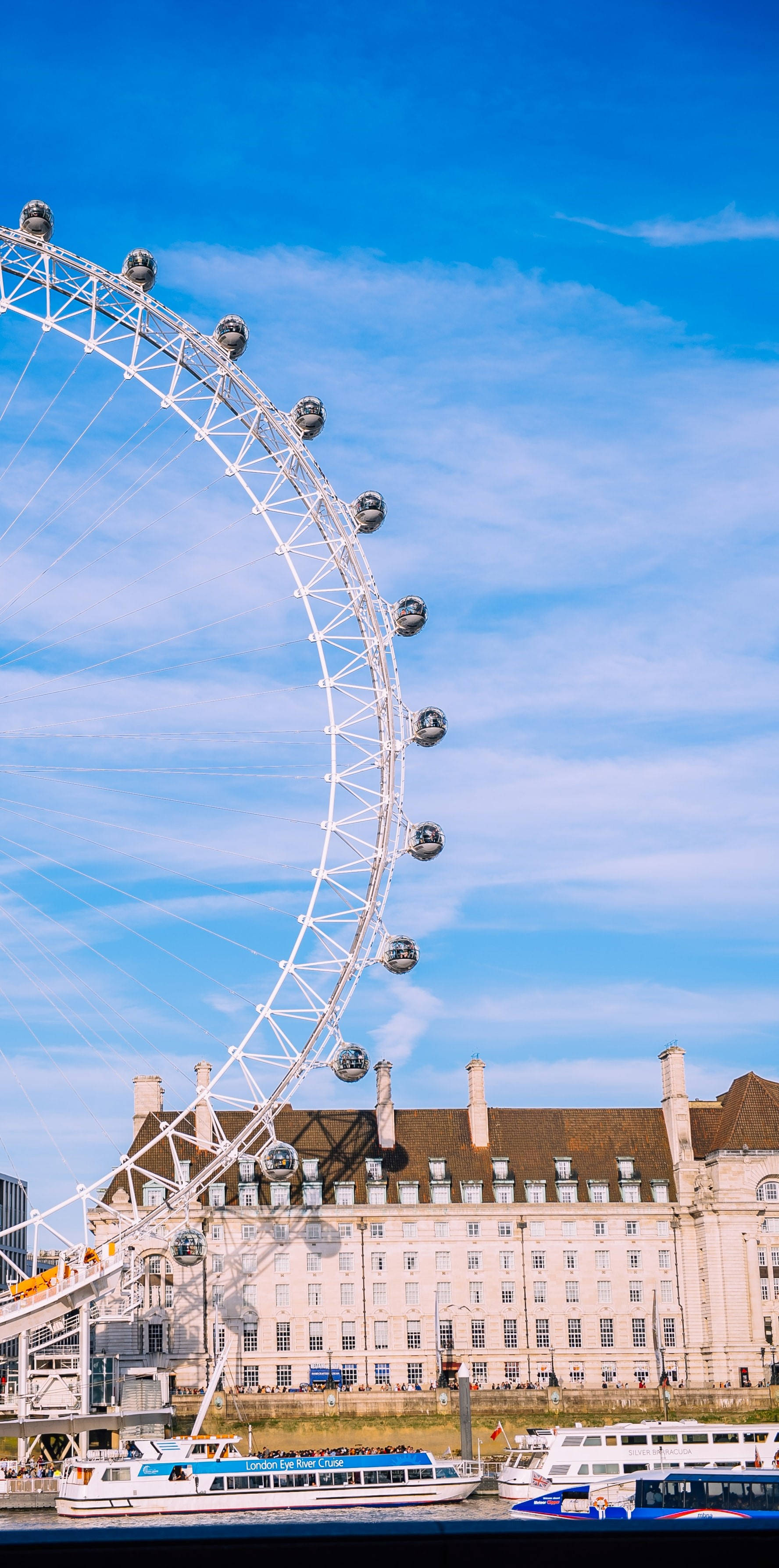 England 桌布 壁紙 — 倫敦眼在泰晤士河上方明亮的藍天下佔據主導地位，下方有船隻和歷史建築。