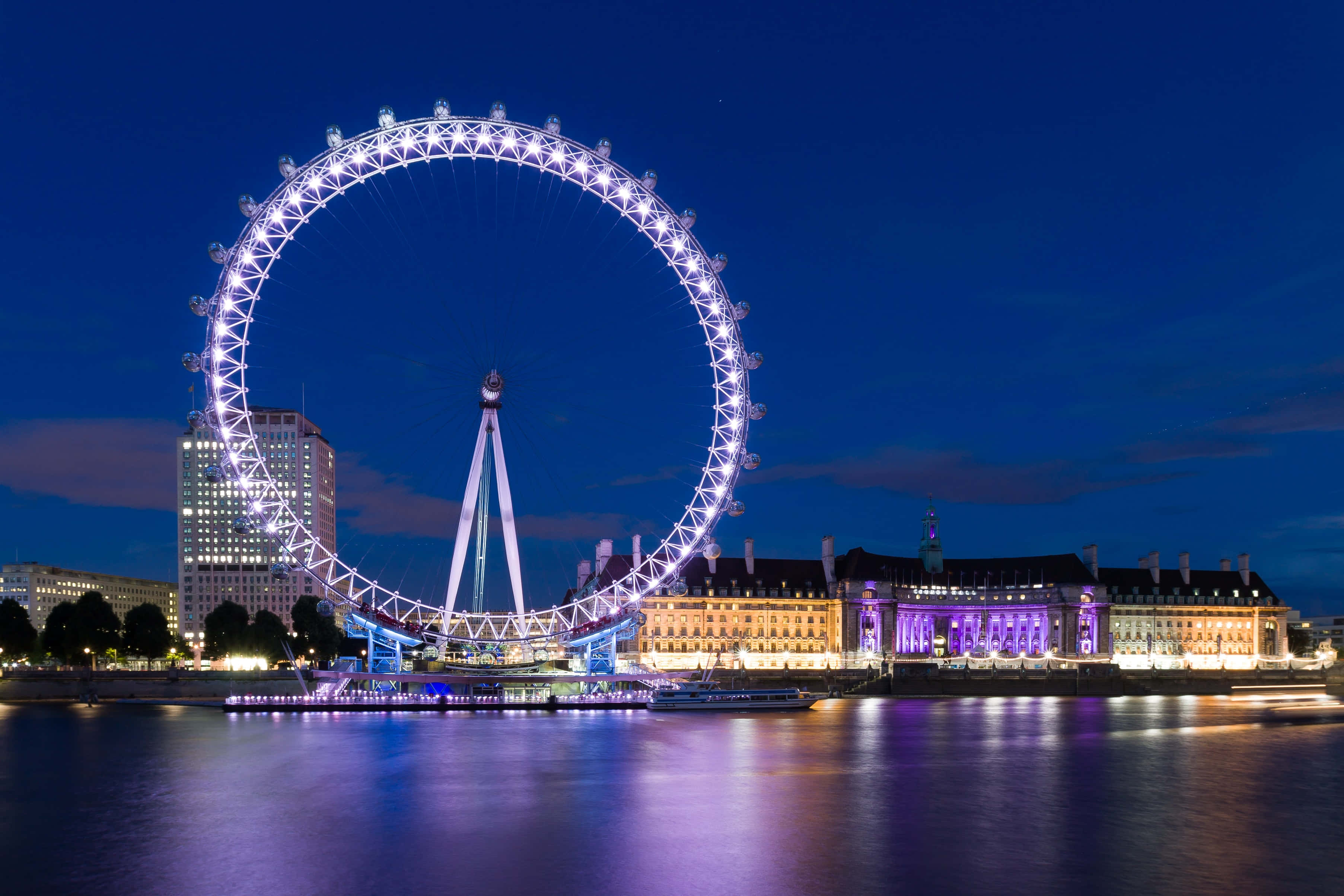 England 桌布 壁紙 — 倫敦眼在深藍色的夜空中發出白色光芒，其倒影在下方平靜的泰晤士河上閃爍。