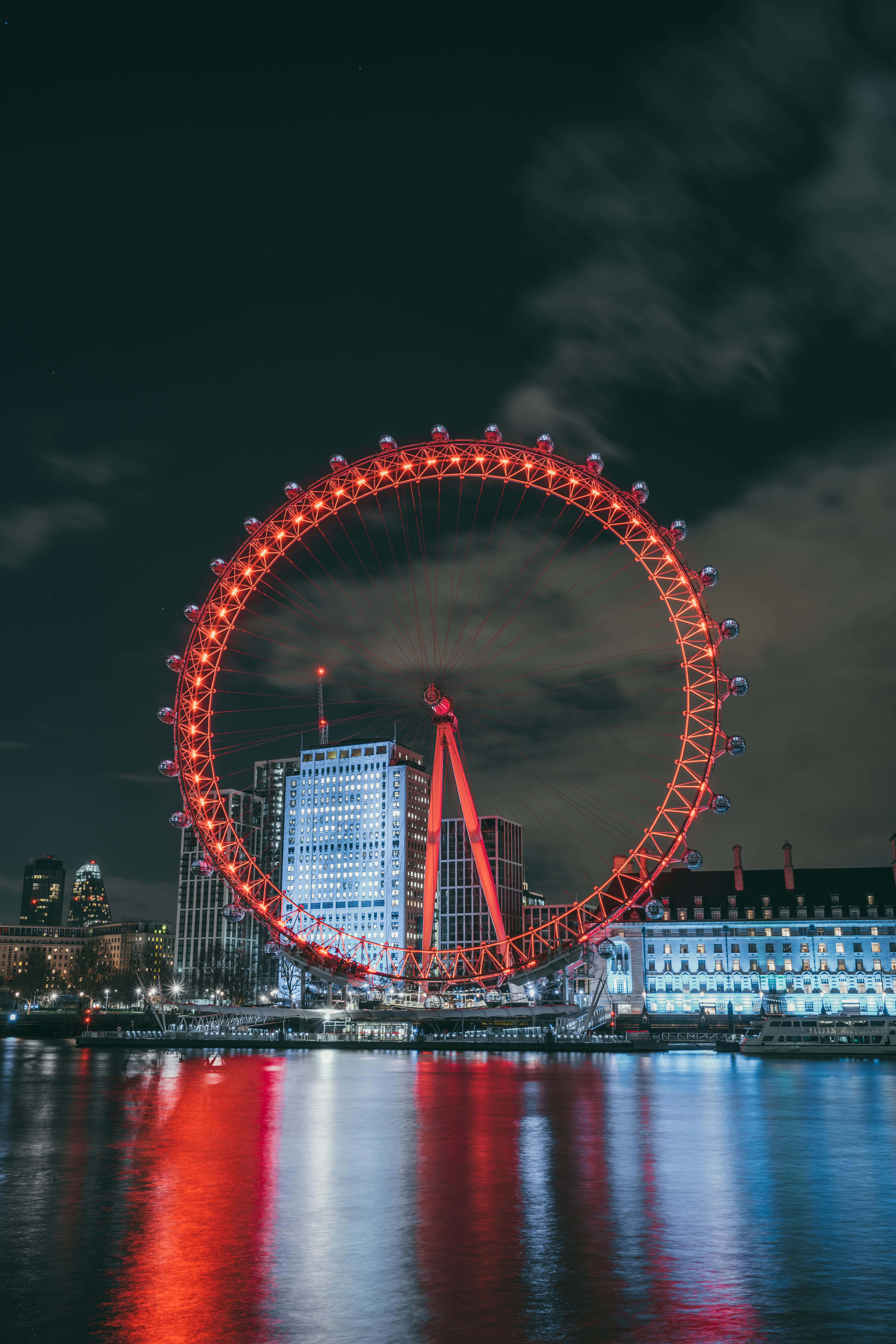 City Lights 桌布 壁紙 — 倫敦眼在漆黑的夜空中發出鮮豔的紅光，其燈光生動地倒映在下方平靜的泰晤士河上。