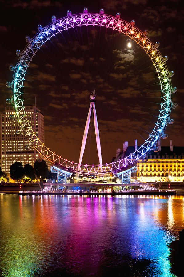 City Lights 桌布 壁紙 — 倫敦眼在繁星點點的夜空下閃爍著彩虹燈光，倒影在泰晤士河上閃閃發光。