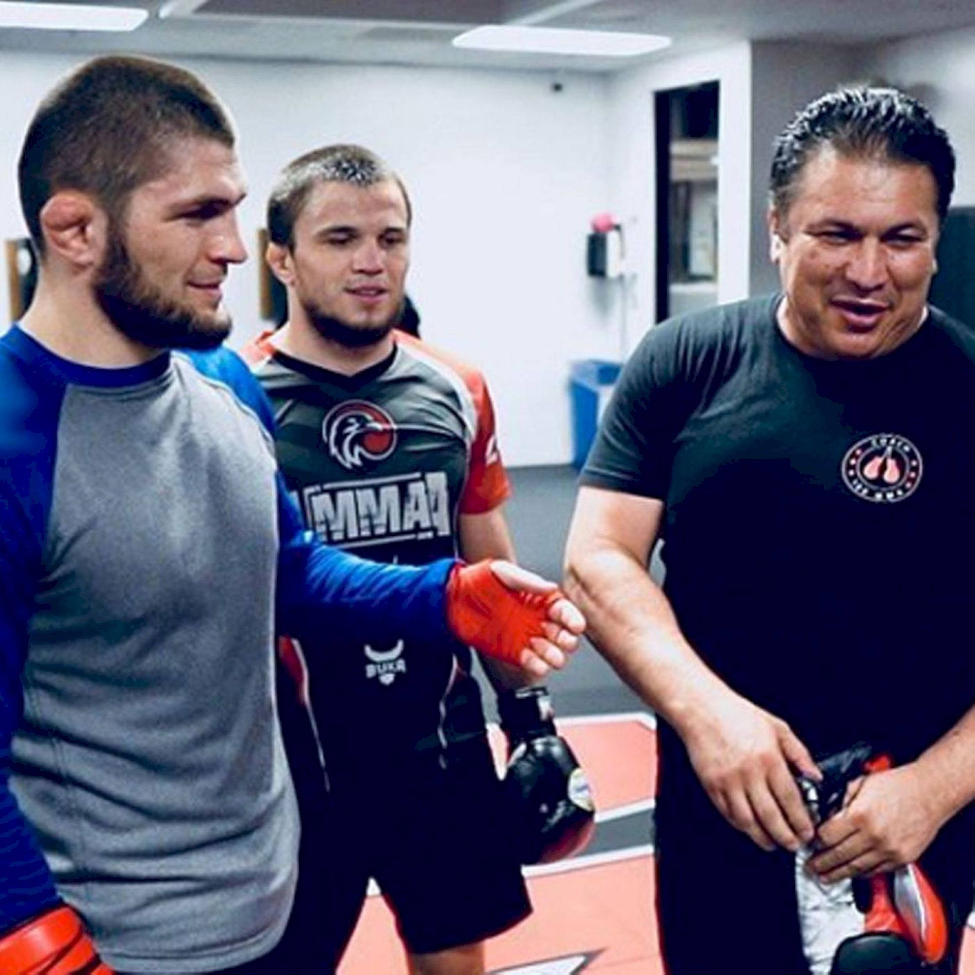 UFC 桌布 壁紙 — 健身房裡有三個男人，一個與另一個握手，第三個微笑著觀看。