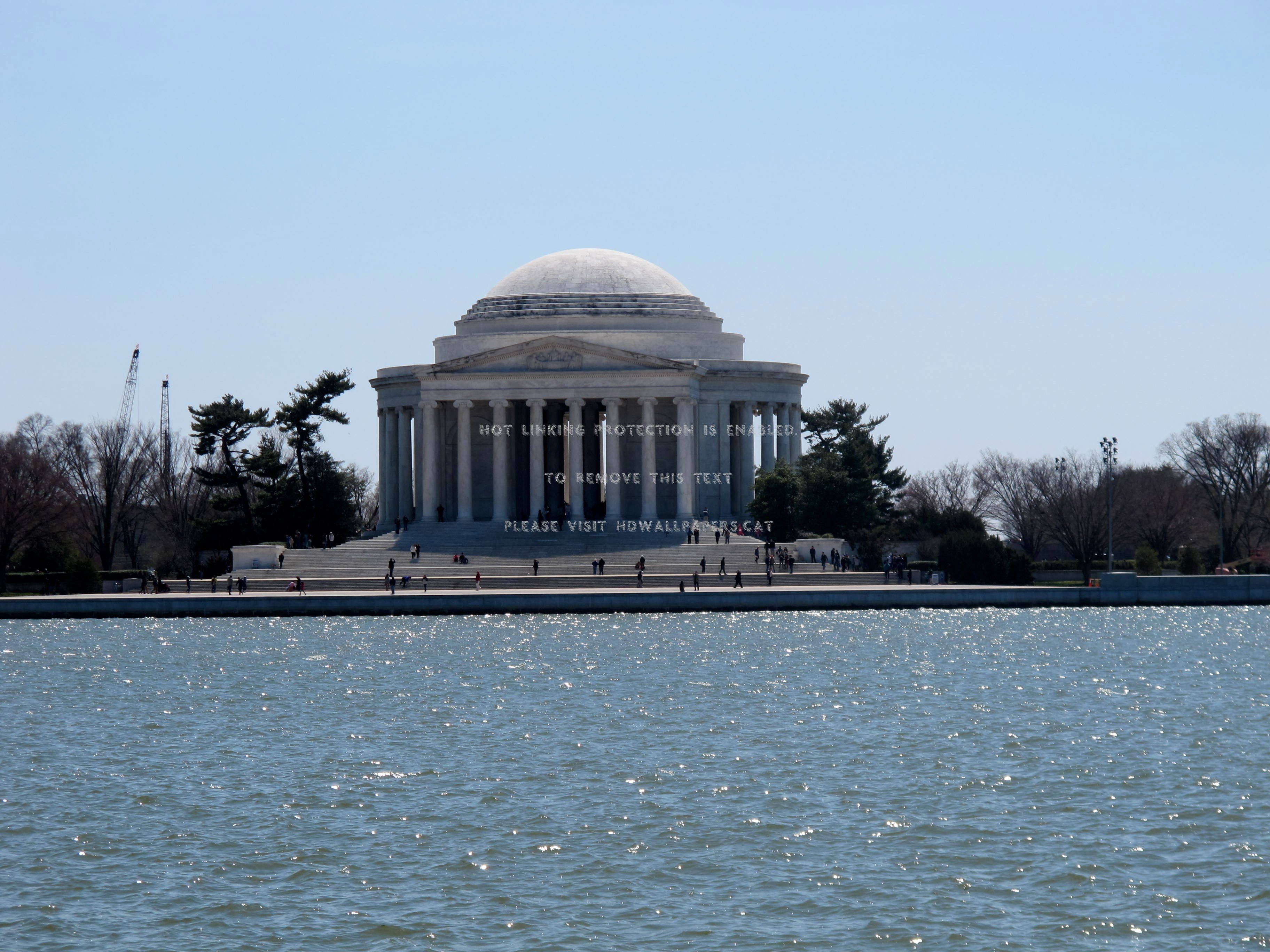 Jefferson Memorial 桌布 壁紙 — 傑佛遜紀念堂雄偉地矗立在潮汐湖上，陽光在水面上閃爍，光禿禿的樹木排列在岸邊。
