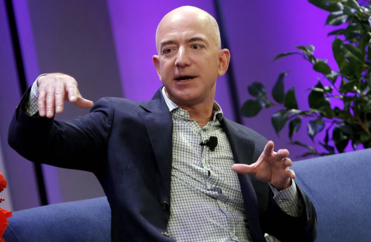 Bezos 桌布 壁紙 — 傑夫·貝佐斯坐在藍色沙發上，在充滿綠色植物的鮮豔紫色背景下生動地做手勢。