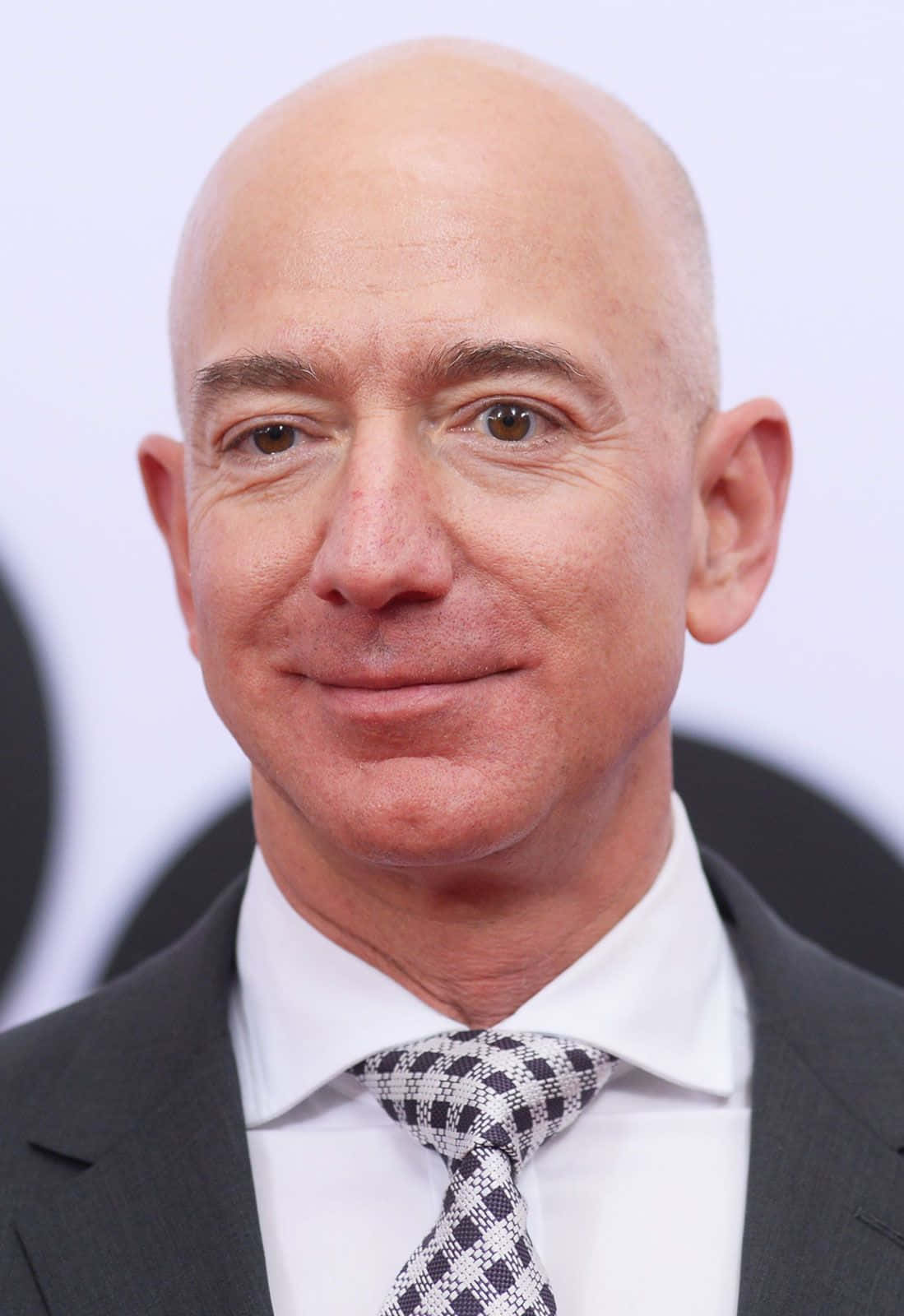 Jeff Bezos 桌布 壁紙 — 傑夫·貝佐斯身穿深色西裝和圖案領帶，背景模糊的頭像特寫。