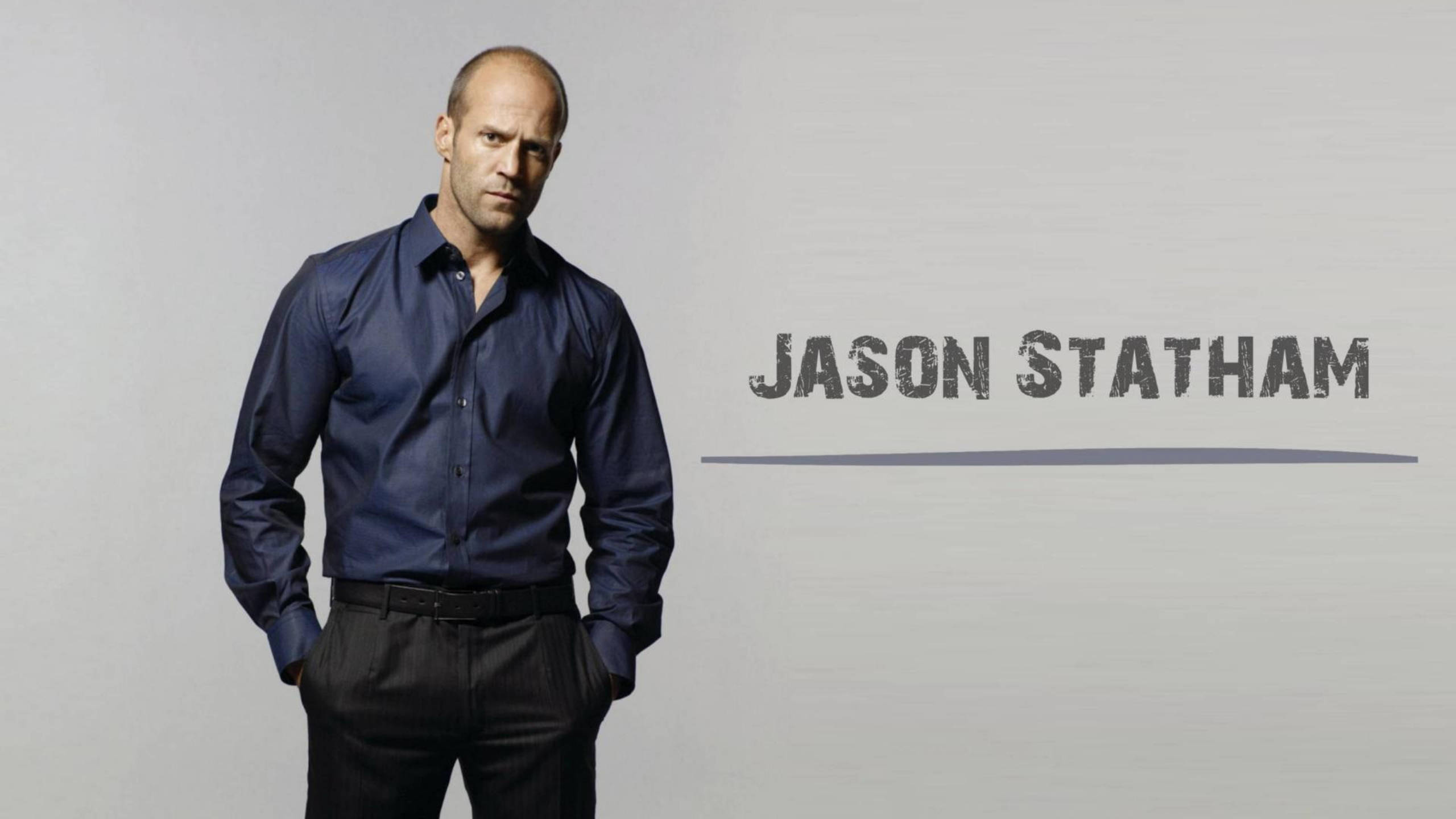 jason 桌布 壁紙 — 傑森·史塔森自信地站在純灰色背景前，身穿深藍色襯衫，他的名字以粗體顯示。