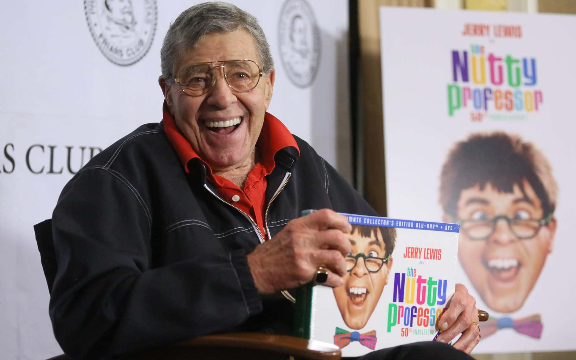 Jerry Lewis 桌布 壁紙 — 傑瑞·路易斯在宣傳活動中手持色彩繽紛的《瘋狂教授》50週年紀念書，滿面笑容。