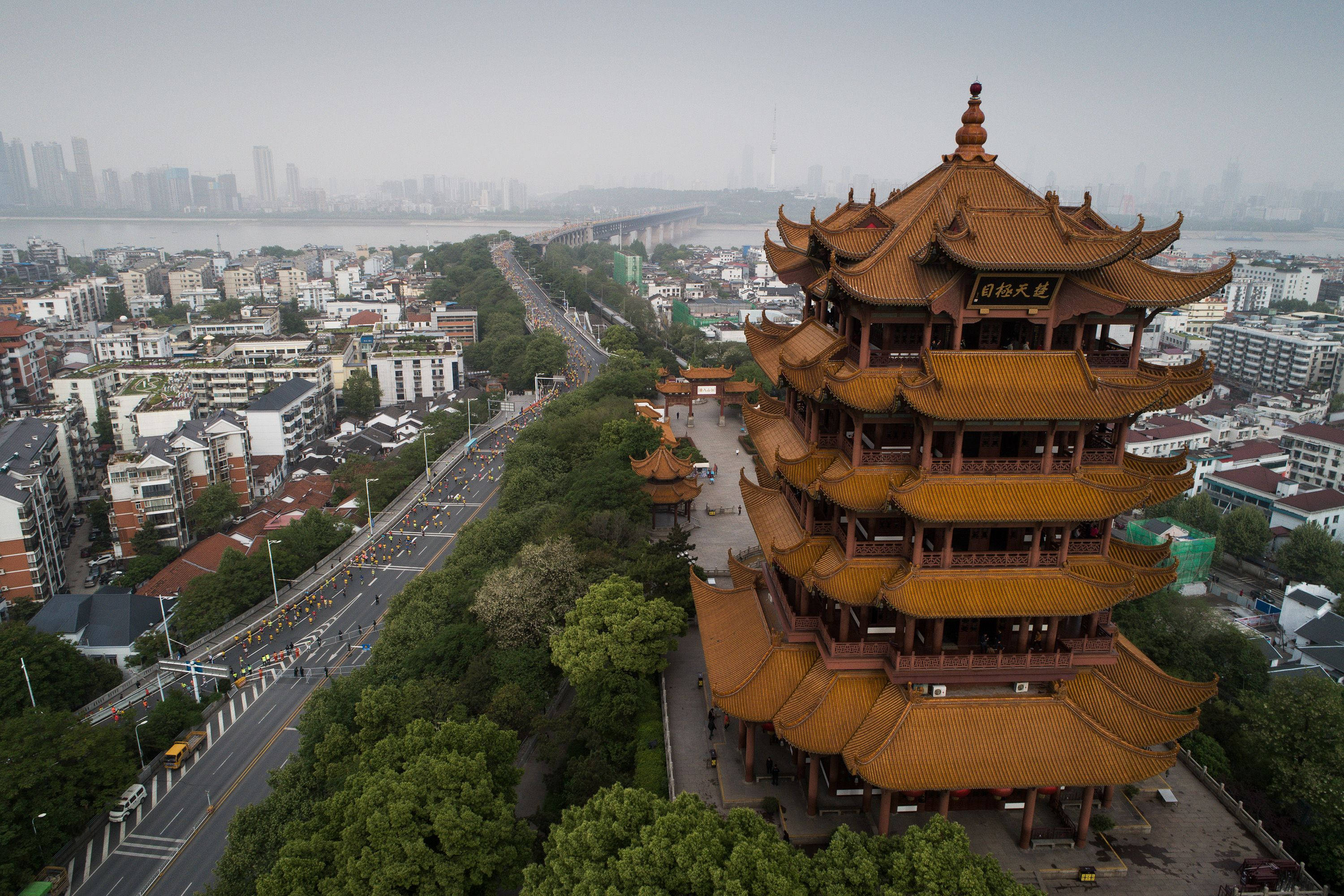 中國 桌布 壁紙 — 傳統中國寶塔的鳥瞰圖，金色屋頂矗立在綠樹叢中，旁邊是繁忙的城市道路和河流，遠處是城市天際線。