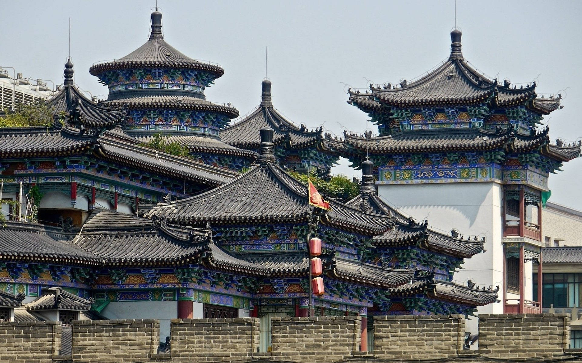 Beijing 桌布 壁紙 — 傳統中國寺廟屋頂帶有精緻的藍色和金色裝飾，在朦朧的天空下聳立於古老的石牆之上。