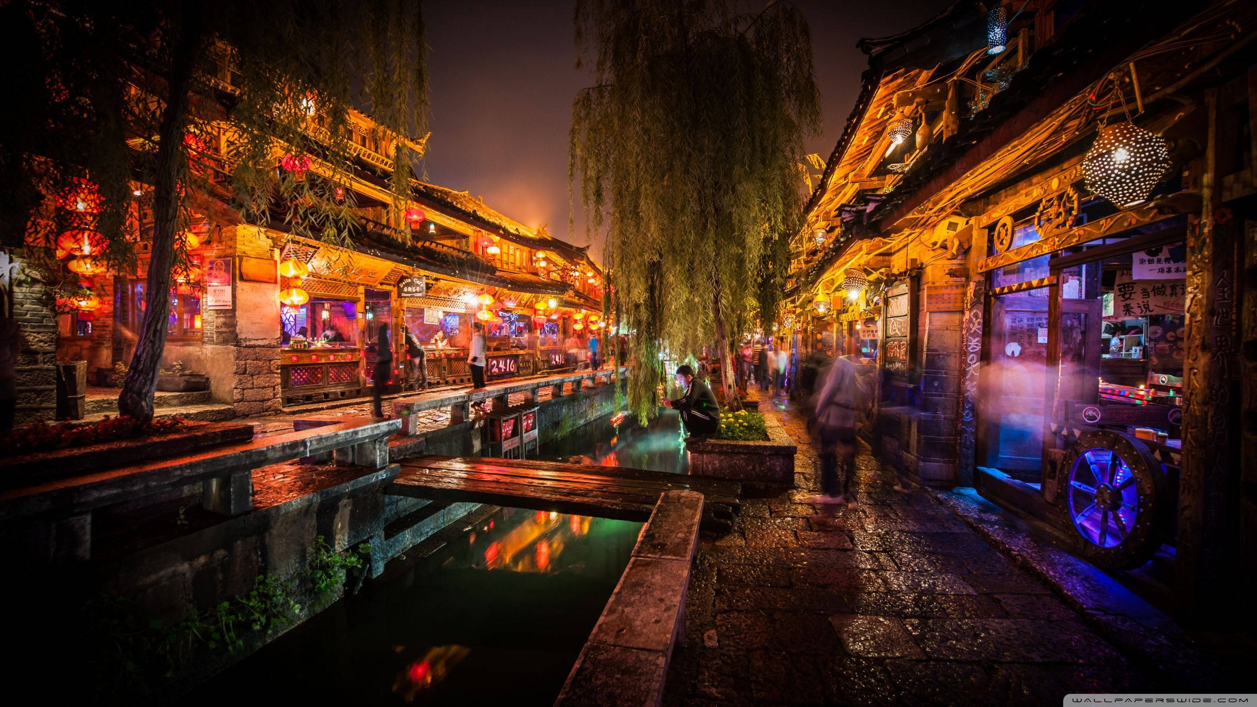 日本 桌布 壁紙 — 傳統中國小鎮運河旁的熱鬧夜景，有發光的燈籠和行人走在濕漉漉的石板路上。