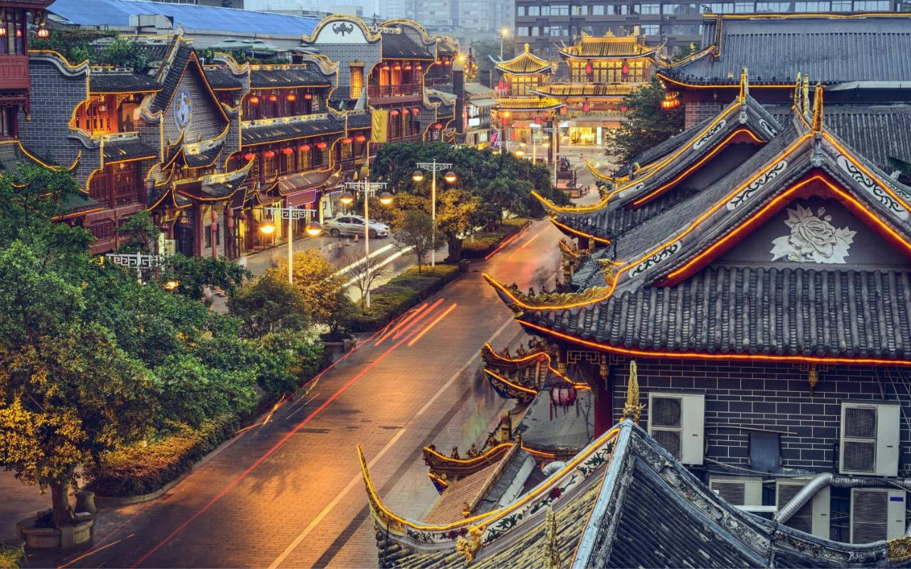 Chengdu 桌布 壁紙 — 傳統中國建築在夜晚閃耀著金色燈光，濕漉漉的街道上模糊的車軌的鳥瞰圖。