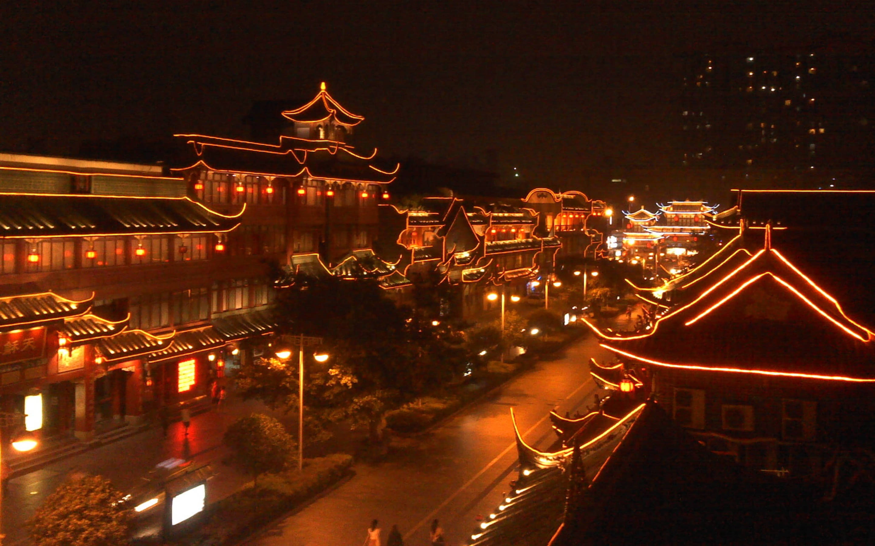 Chengdu 桌布 壁紙 — 傳統中國建築在繁華街道上閃爍著溫暖橙色燈光的夜間鳥瞰圖。