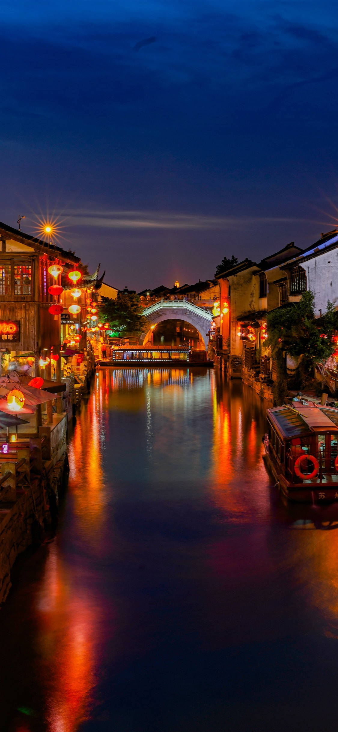 Suzhou 桌布 壁紙 — 傳統中國水鄉中一條寧靜的黃昏運河，燈籠的光芒在深藍色天空下映照在平靜的水面上。
