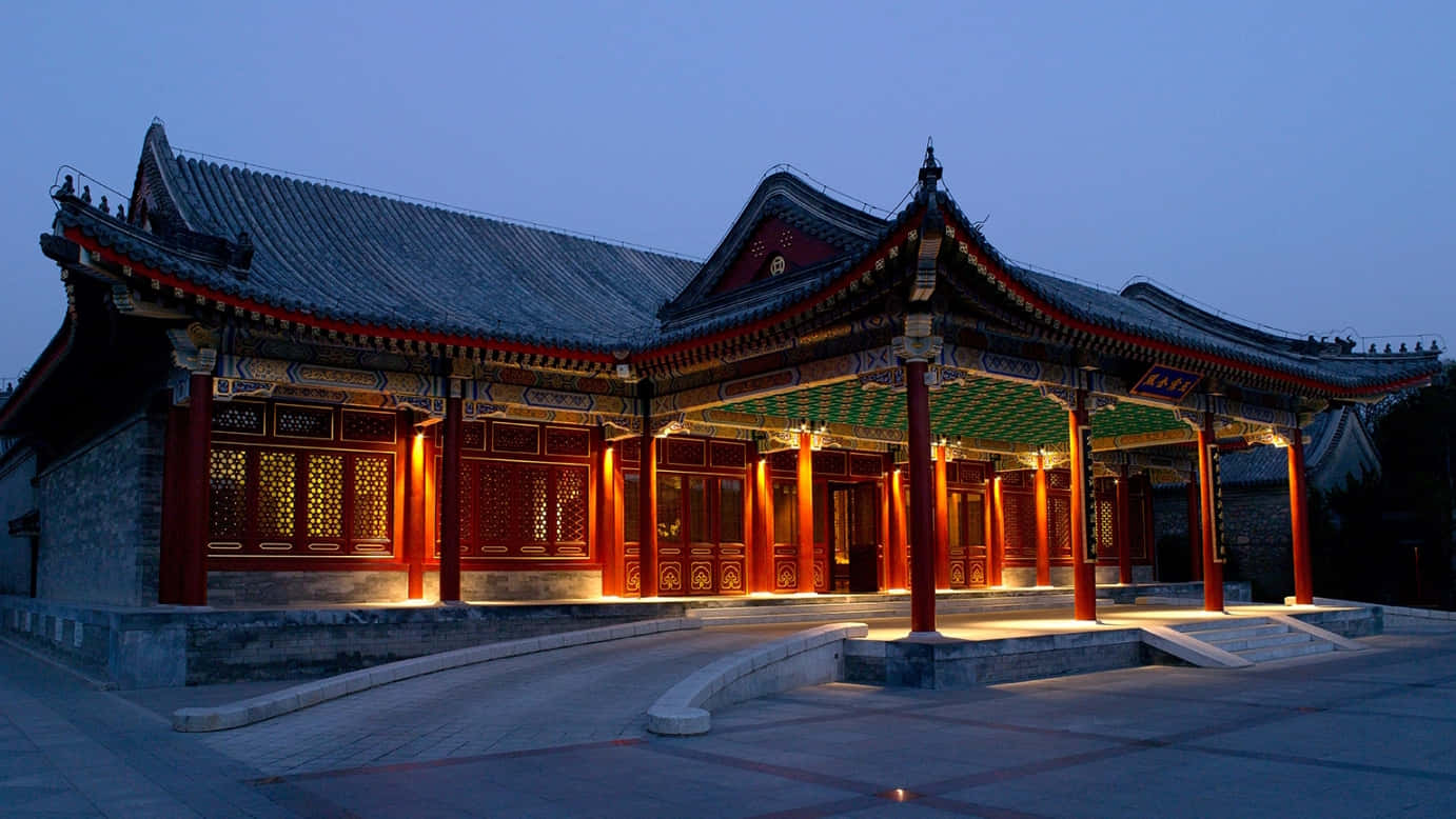 建築 桌布 壁紙 — 傳統中式亭閣，紅色柱子和瓦片屋頂在傍晚燈光下溫暖地發光，映襯著深藍色的天空。
