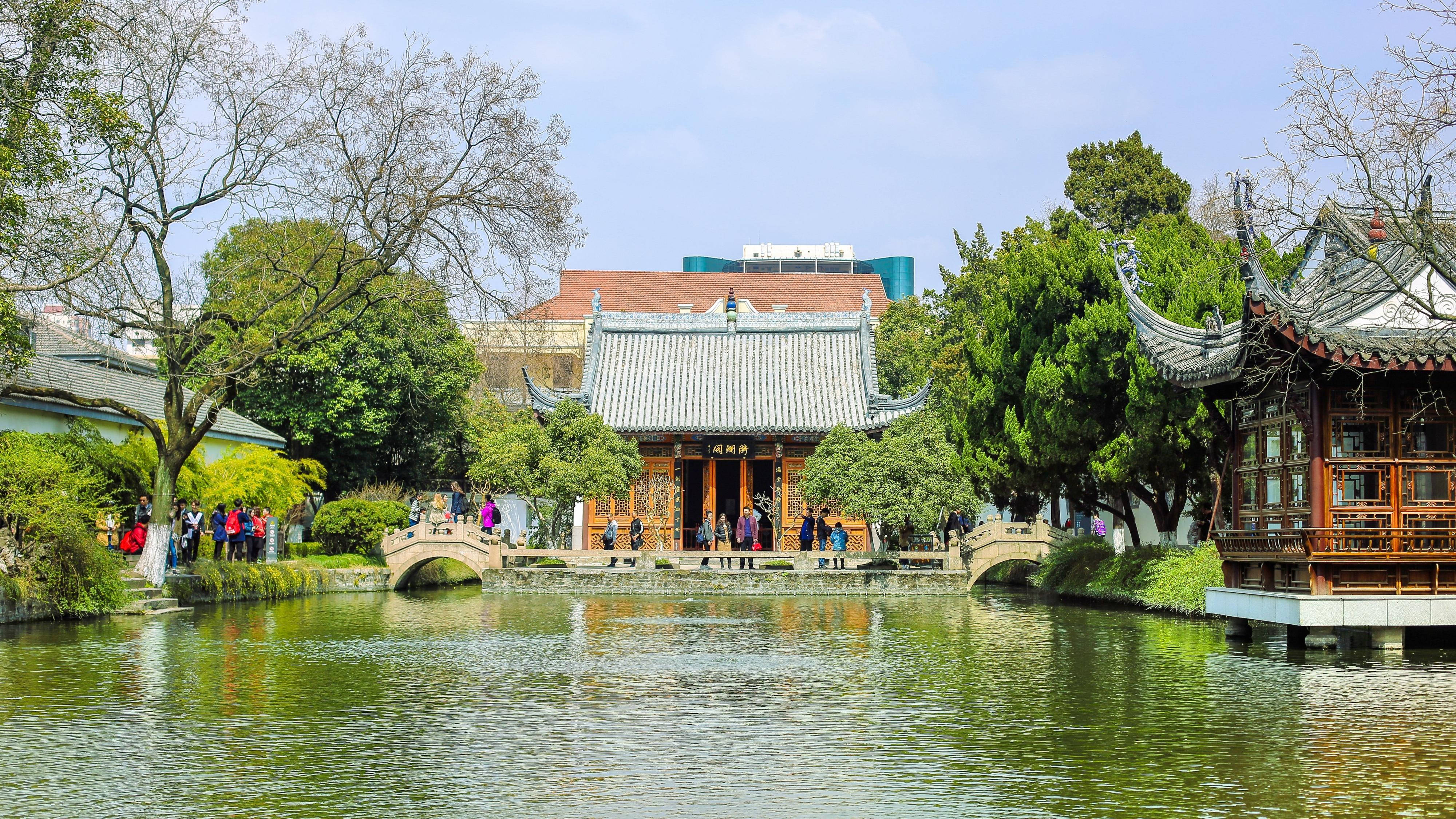 Nanjing 桌布 壁紙 — 傳統中式亭閣和拱橋倒映在平靜的水面上，四周環繞著茂密的綠植和遊客。