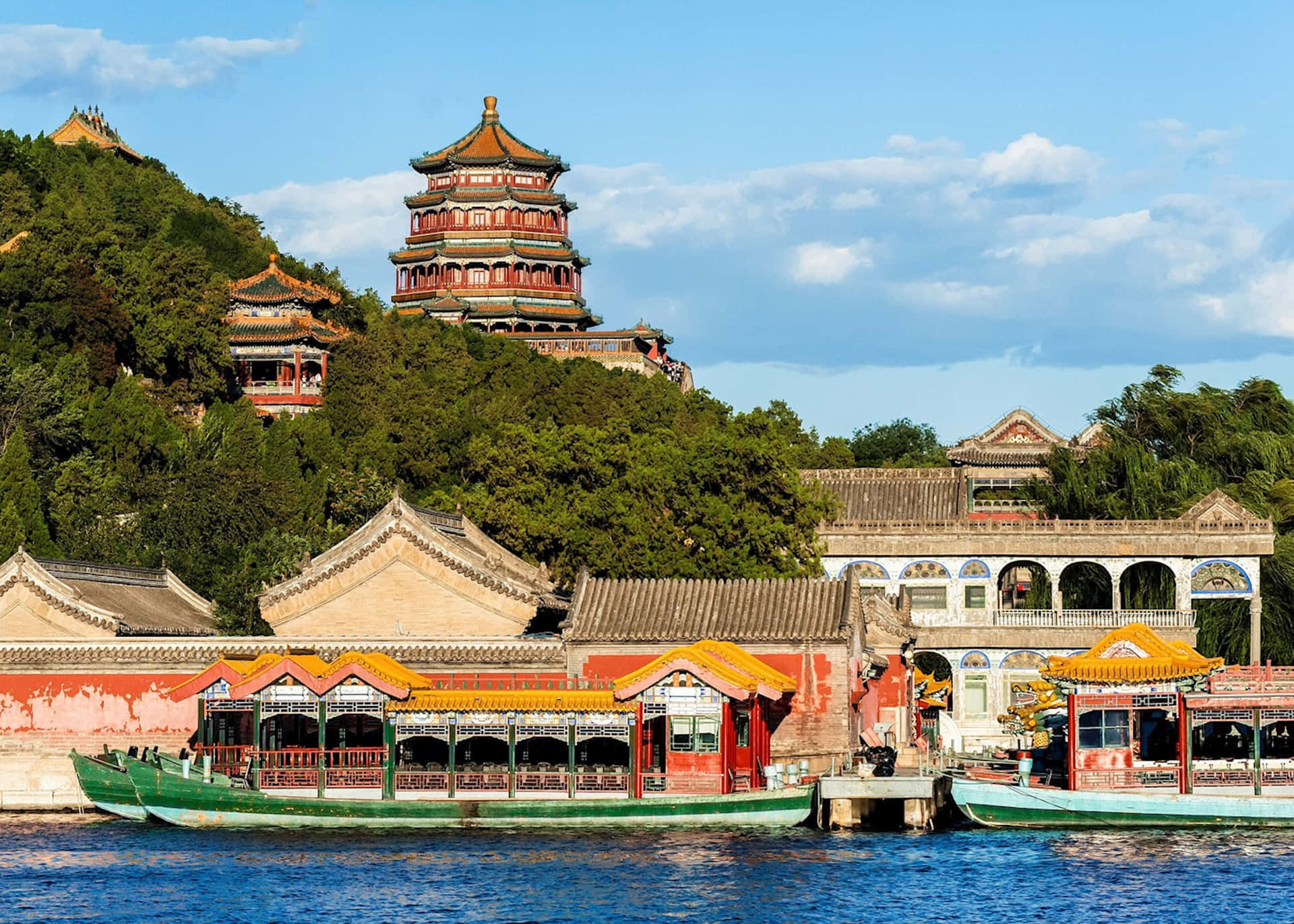 Boating 桌布 壁紙 — 傳統中式宮殿建築，紅瓦金飾，從鬱鬱蔥蔥的青山中拔地而起，旁邊是平靜的藍色湖泊，湖中停泊著船隻。