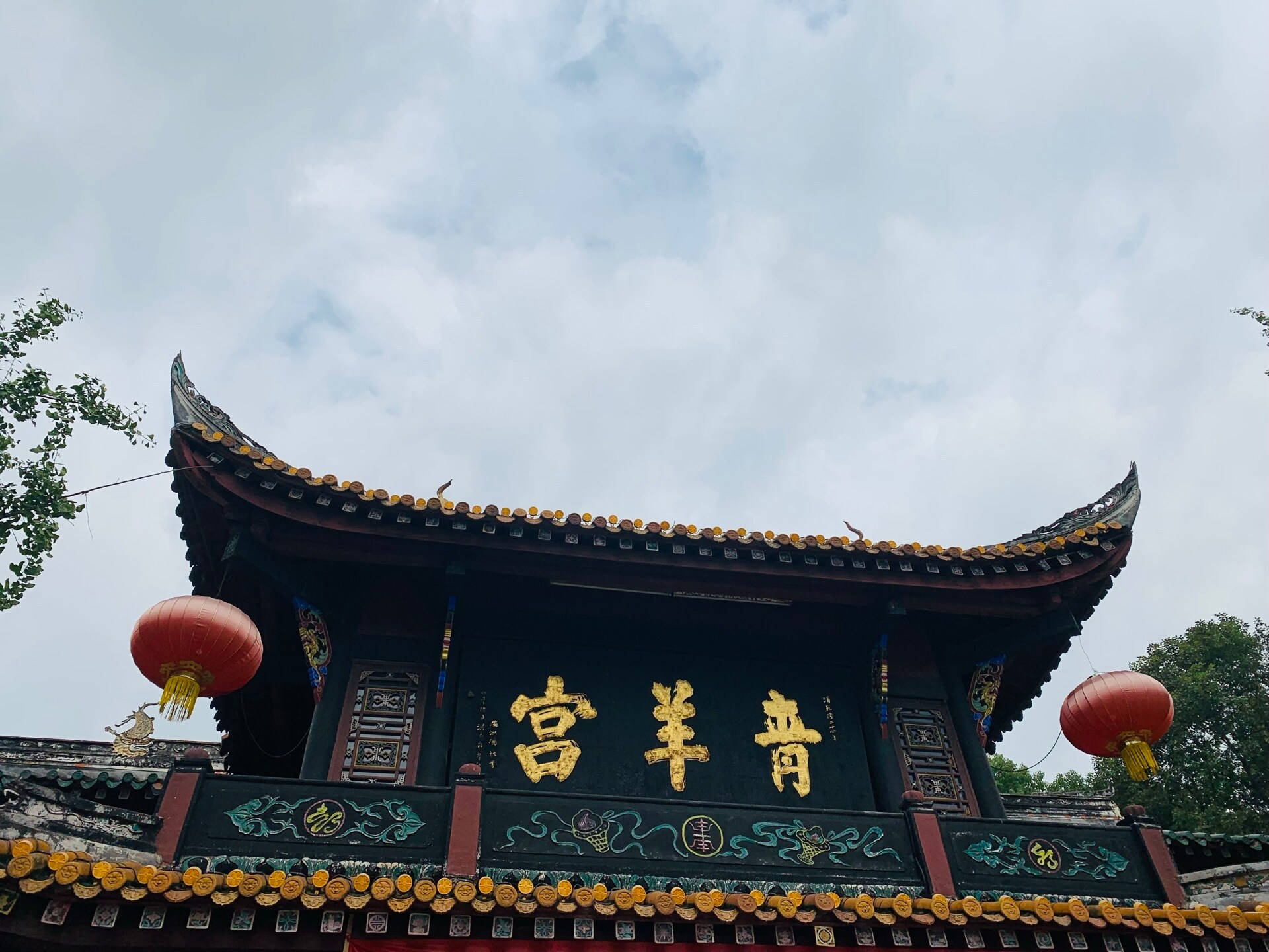 Chengdu 桌布 壁紙 — 傳統中式寺廟，擁有彎曲的屋簷、金色字體和紅色燈籠，天空多雲。