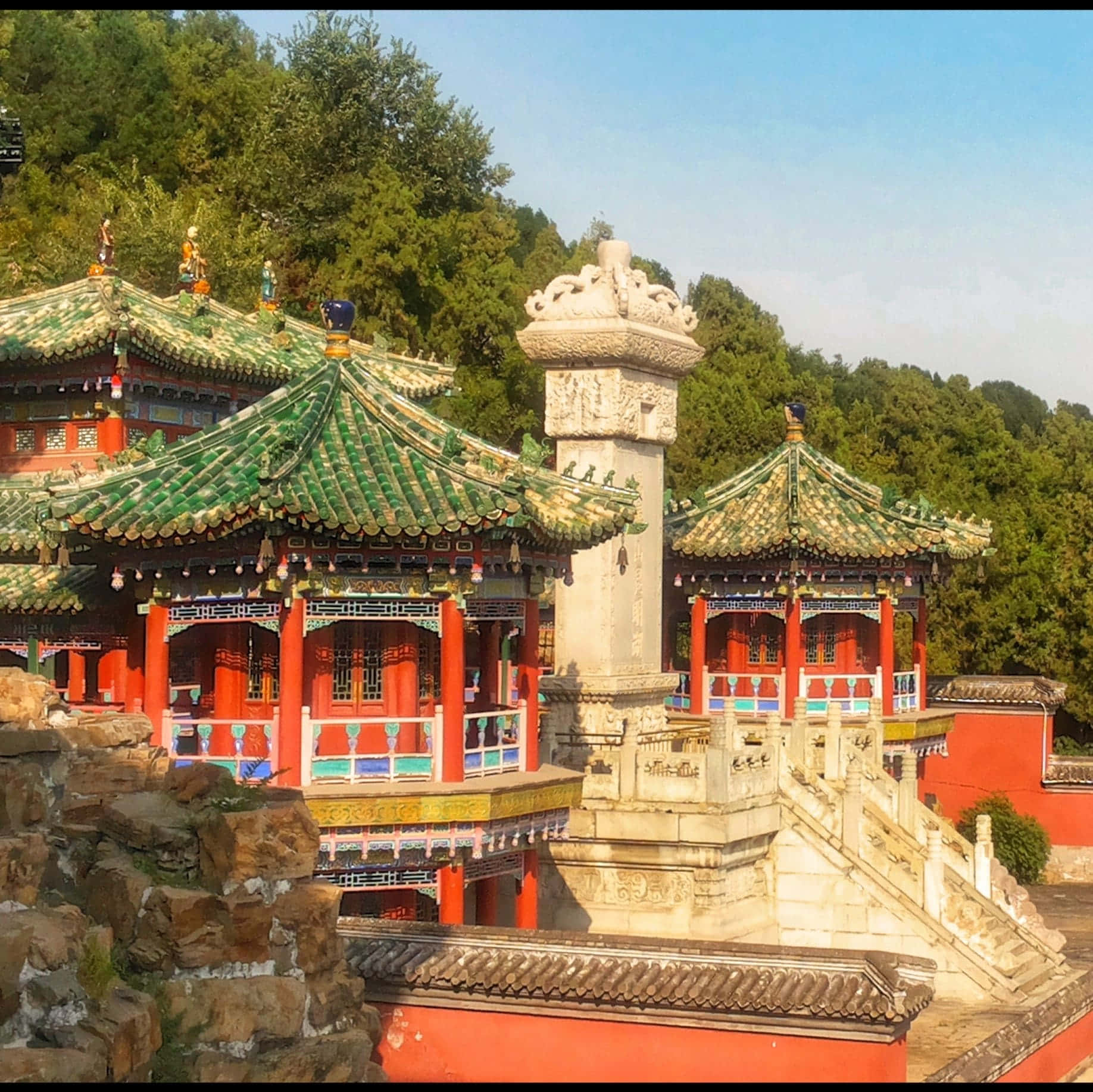 樹木 桌布 壁紙 — 傳統中式寺廟，綠色瓦頂和紅色柱子，坐落在茂密的綠樹叢中，天空清澈湛藍。