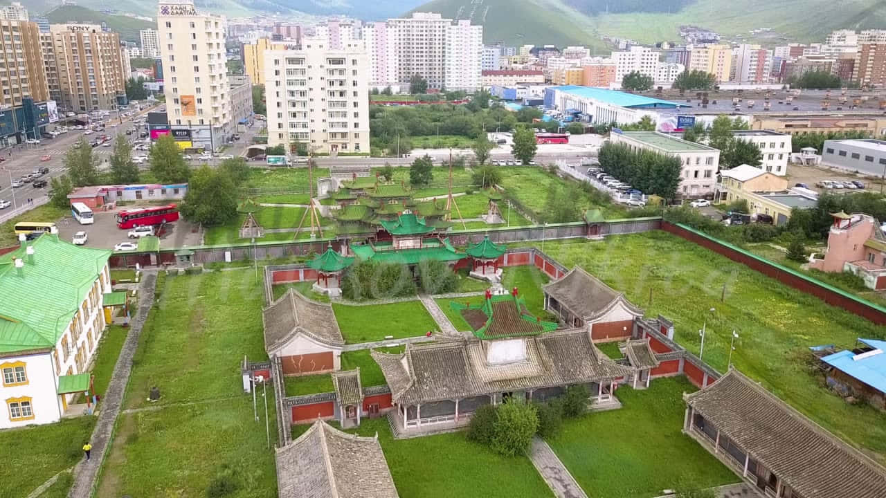 Mongolia 桌布 壁紙 — 傳統中式寺廟建築群的鳥瞰圖，綠色屋頂坐落在草地上，周圍是現代城市建築和遠山。