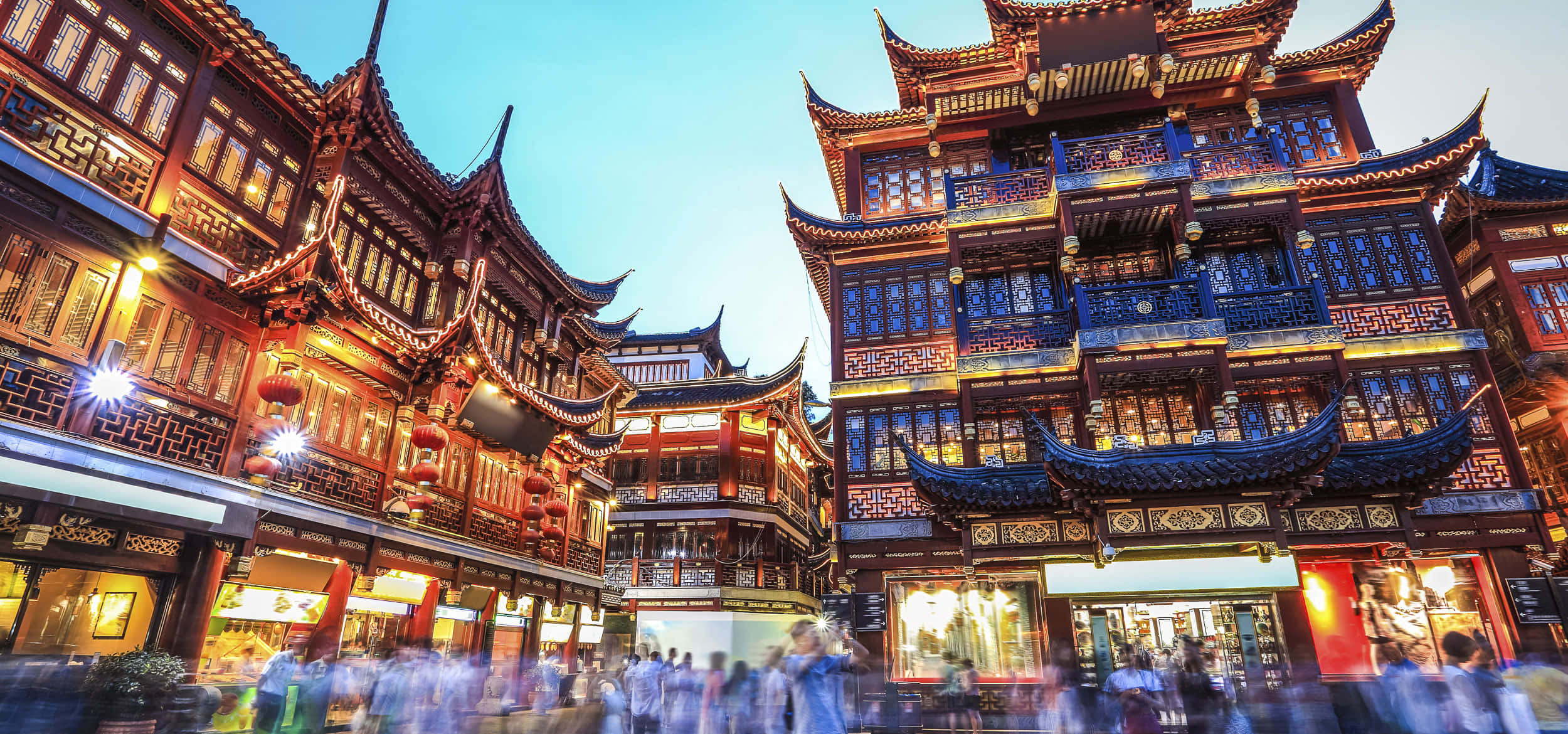 中國 桌布 壁紙 — 傳統中式建築在暮色天空下溫暖地發光，模糊的人群在繁華的歷史街道上移動。