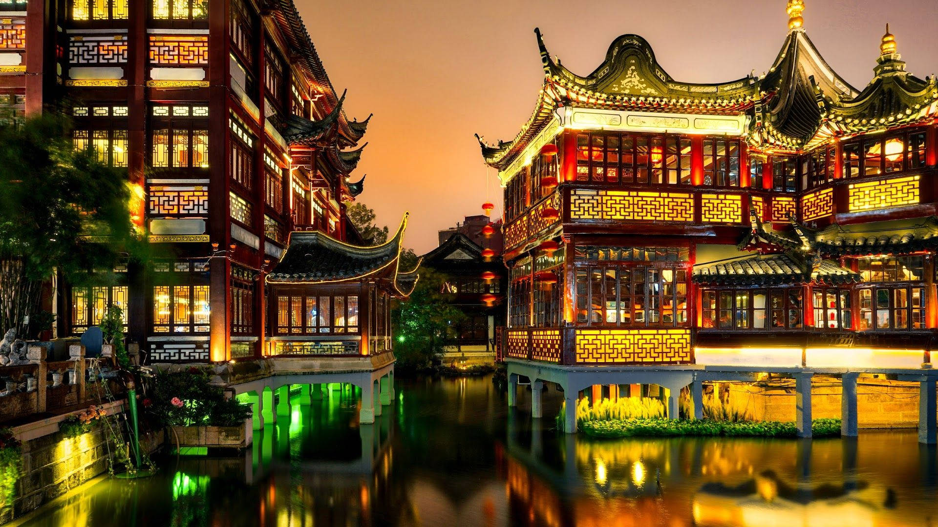 Shanghai 桌布 壁紙 — 傳統中式建築在黃昏時分溫暖地發光，其精緻的屋頂和燈籠倒映在寧靜的運河中。