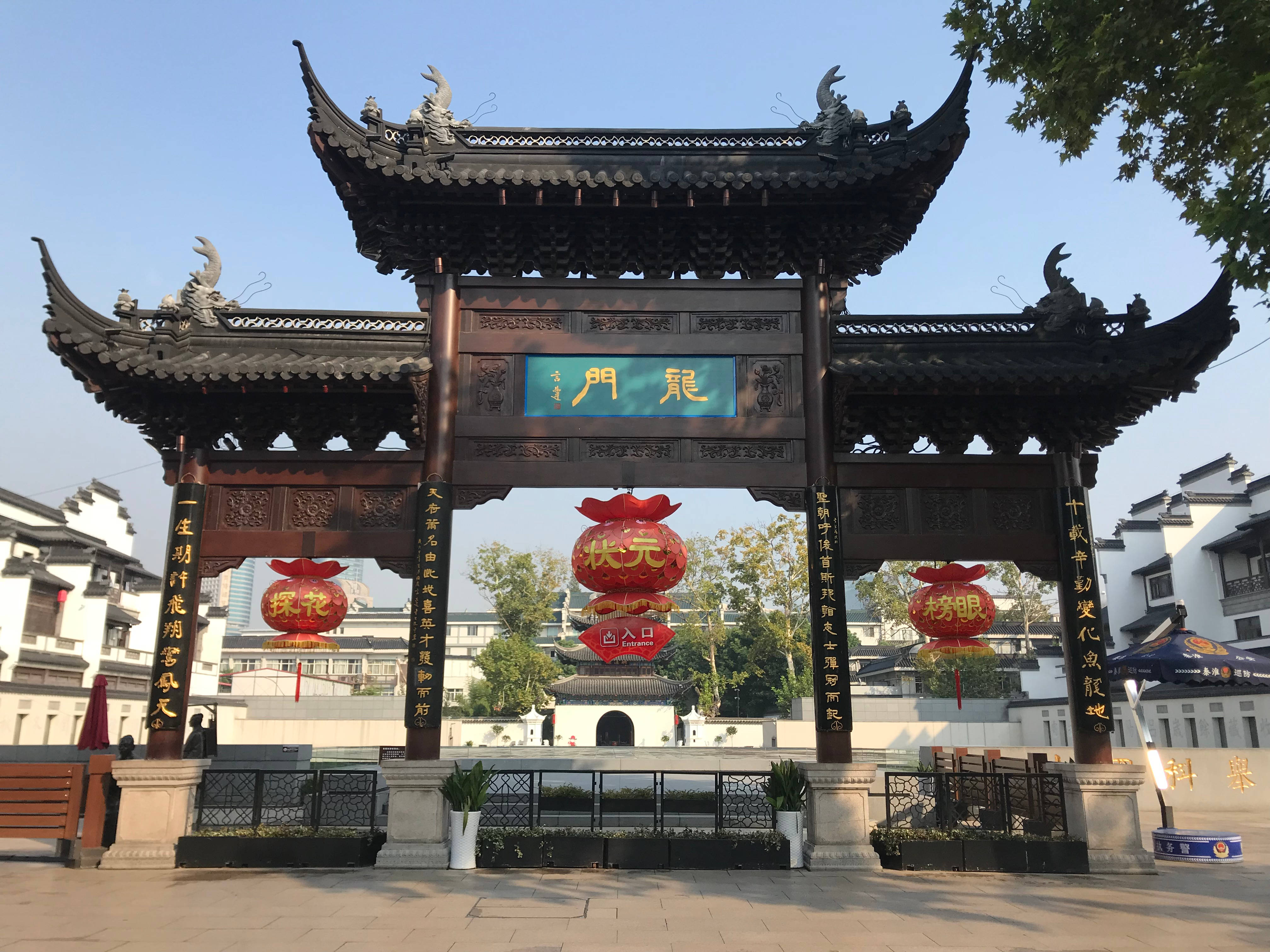 Nanjing 桌布 壁紙 — 傳統中式門樓，帶有彎曲的屋簷和紅色燈籠，矗立在歷史城鎮廣場的藍天白雲下。