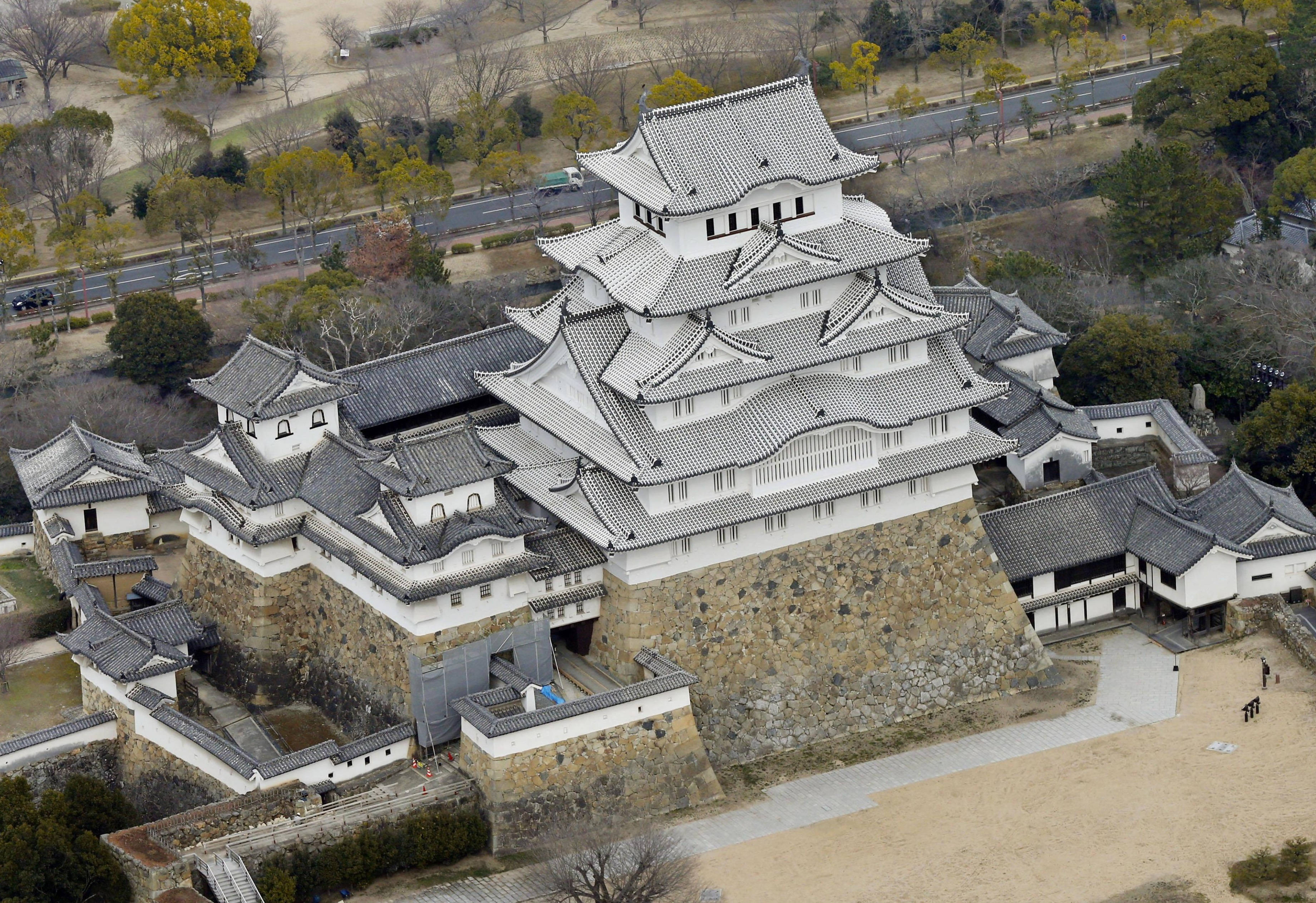 Himeji Castle 桌布 壁紙 — 傳統日本城堡的鳥瞰圖，白色牆壁和灰色瓦片屋頂，周圍有稀疏的樹木和一條道路。