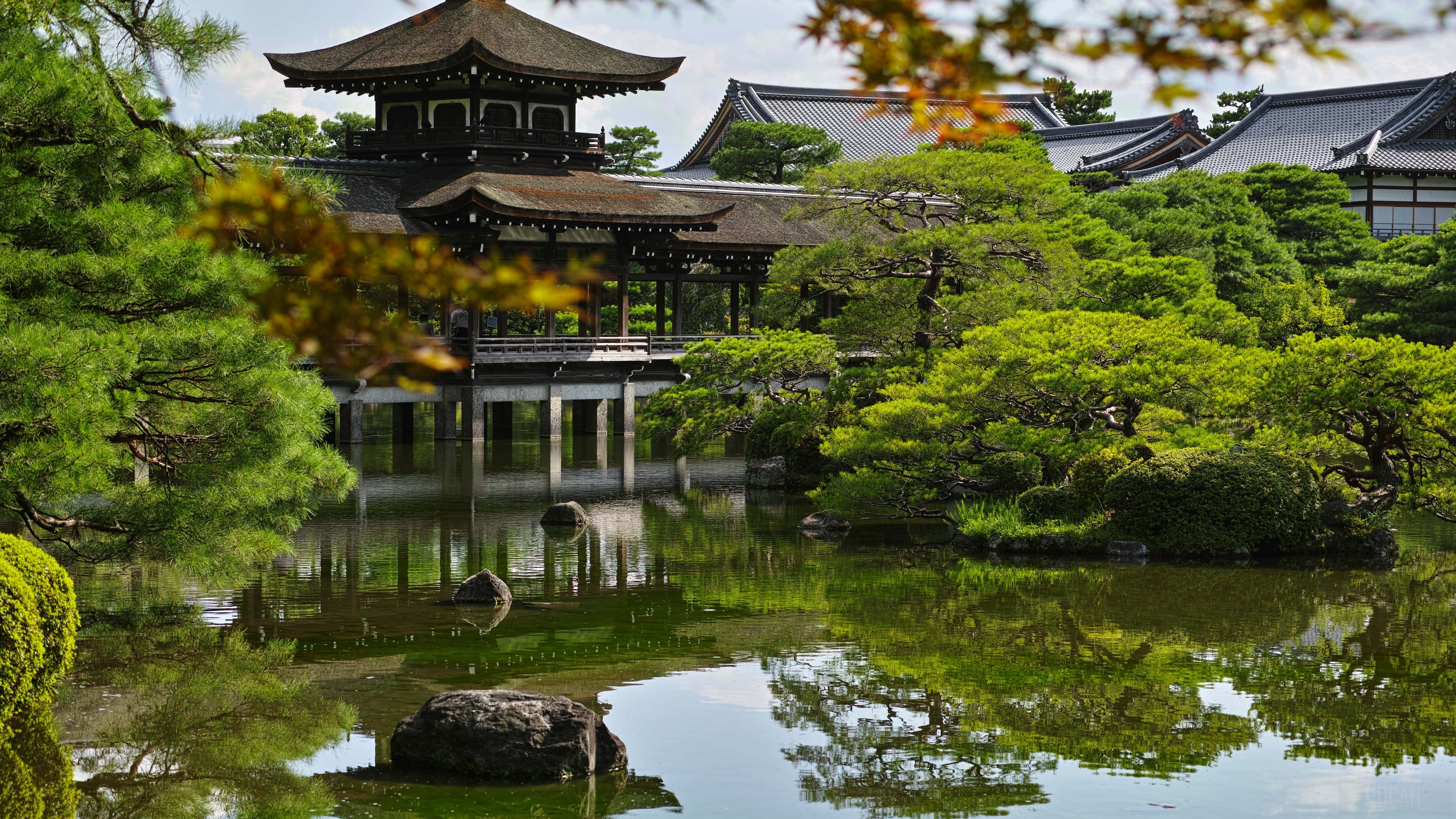 日本 桌布 壁紙 — 傳統日本寺廟亭閣在寧靜的池塘中平靜地倒映，周圍環繞著茂密的綠植和秋色葉子。