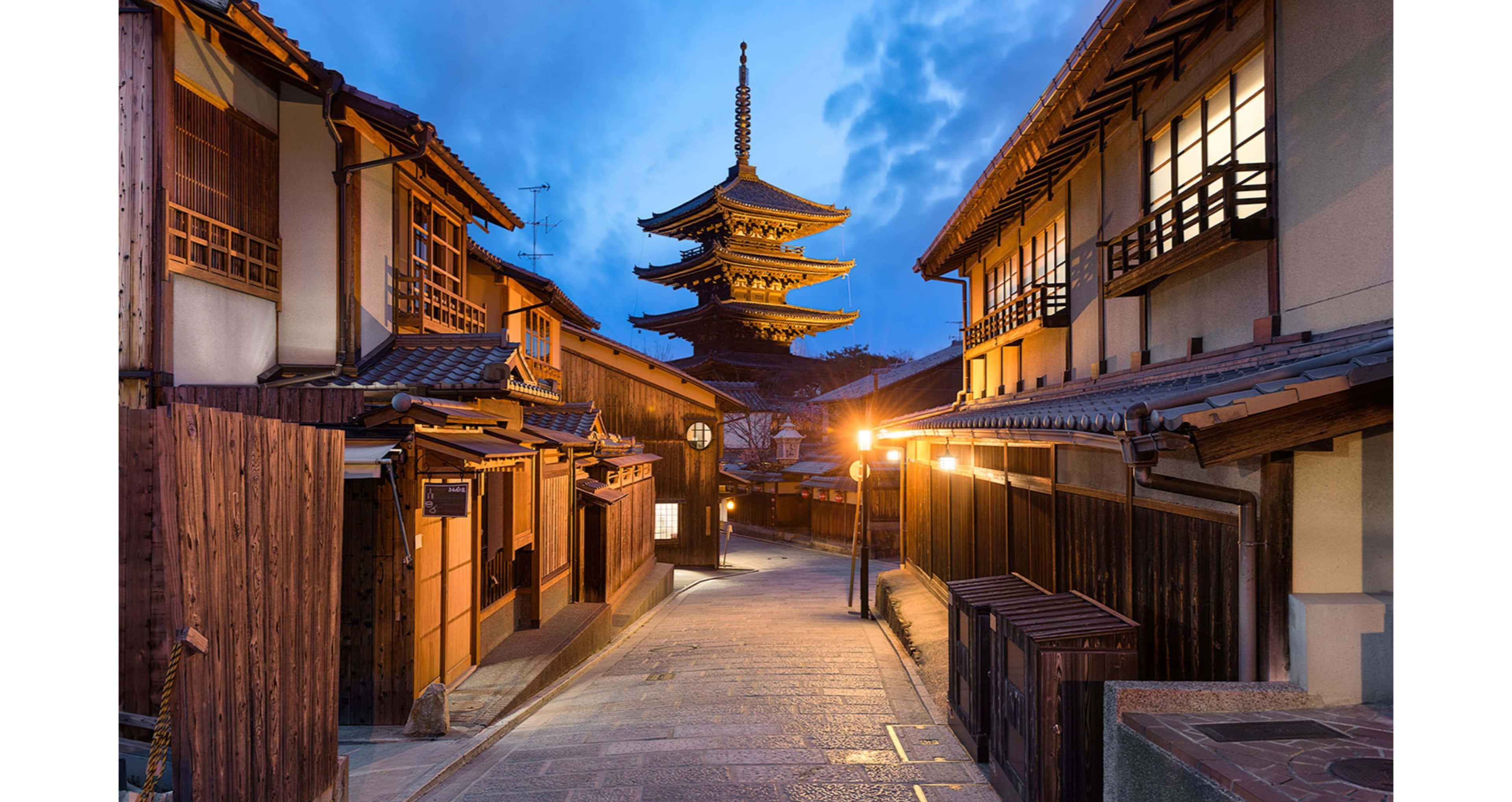日本 桌布 壁紙 — 傳統日本小鎮中一條狹窄的燈籠小巷，通往暮色天空下高聳的寶塔。