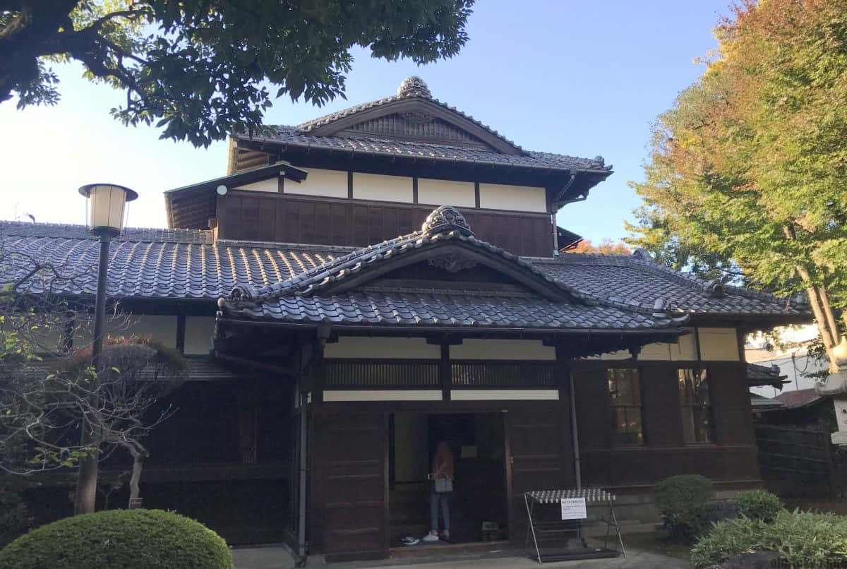 Tokyo Japan 桌布 壁紙 — 傳統日本木屋，深色瓦頂白牆，被秋樹環繞，在清澈藍天下。