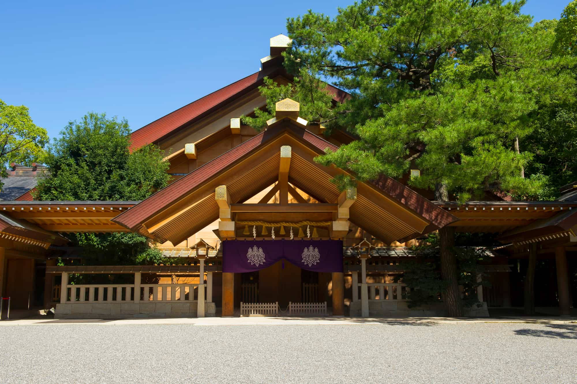 Nagoya 桌布 壁紙 — 傳統日本神社，木造建築與紅色屋頂，被茂密綠樹環繞，天空清澈湛藍。