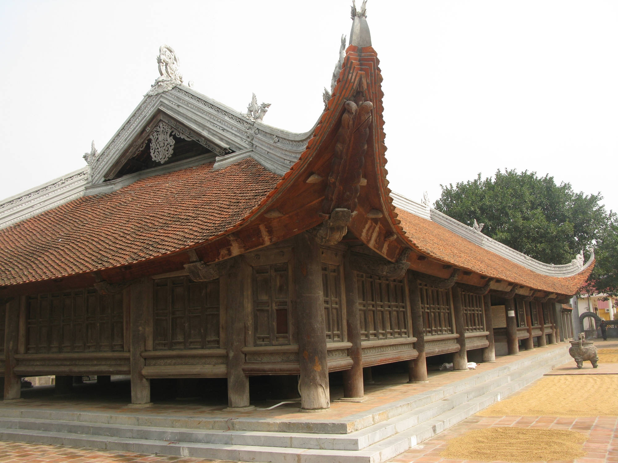 Hanoi 桌布 壁紙 — 傳統木造寺廟，擁有彎曲的紅色瓦頂和華麗的白色飾邊，在陰天之下。