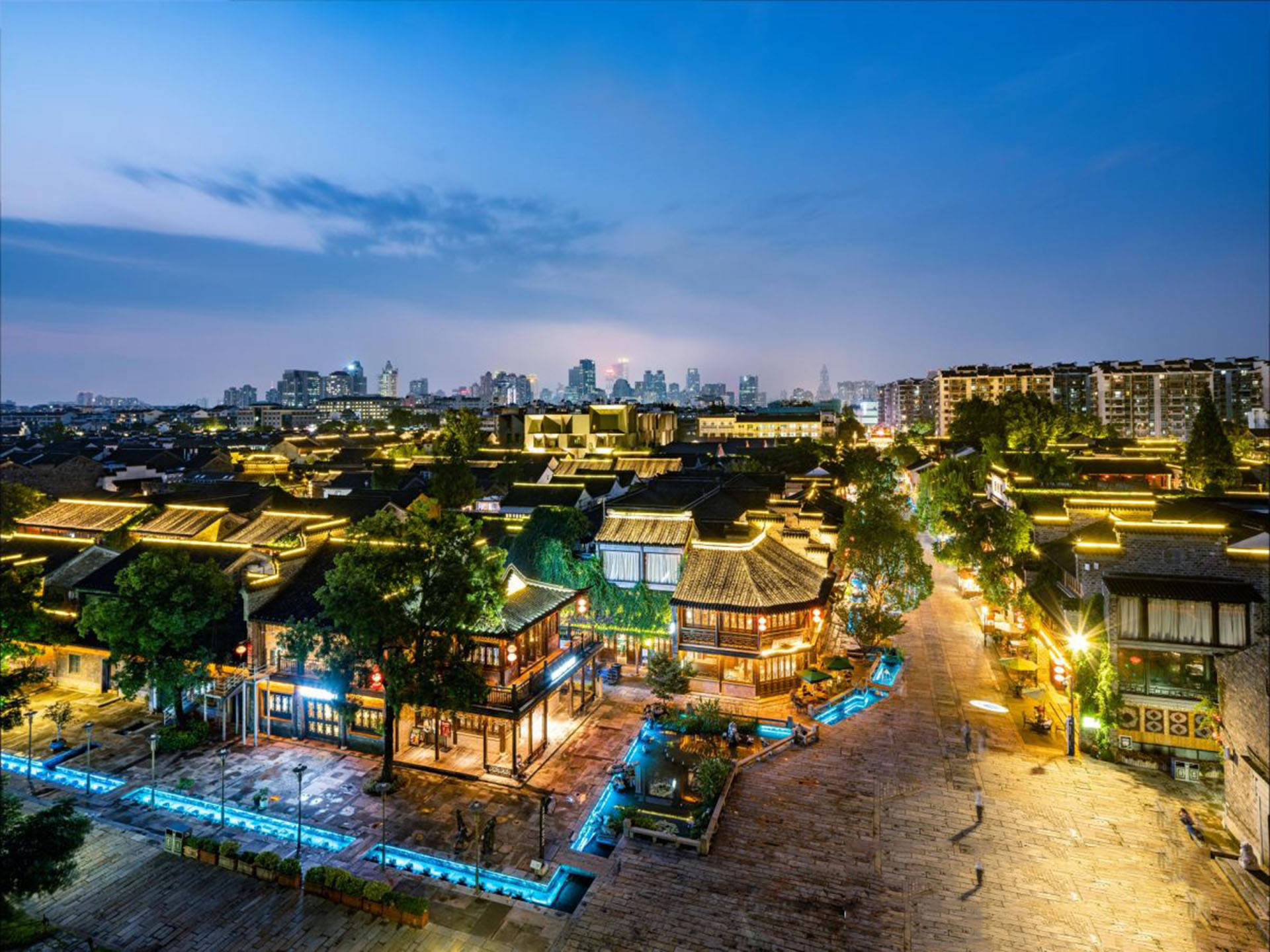 Nanjing 桌布 壁紙 — 傳統瓦頂建築的鳥瞰圖，在暮色天空下散發溫暖燈光，遠方有現代摩天大樓。