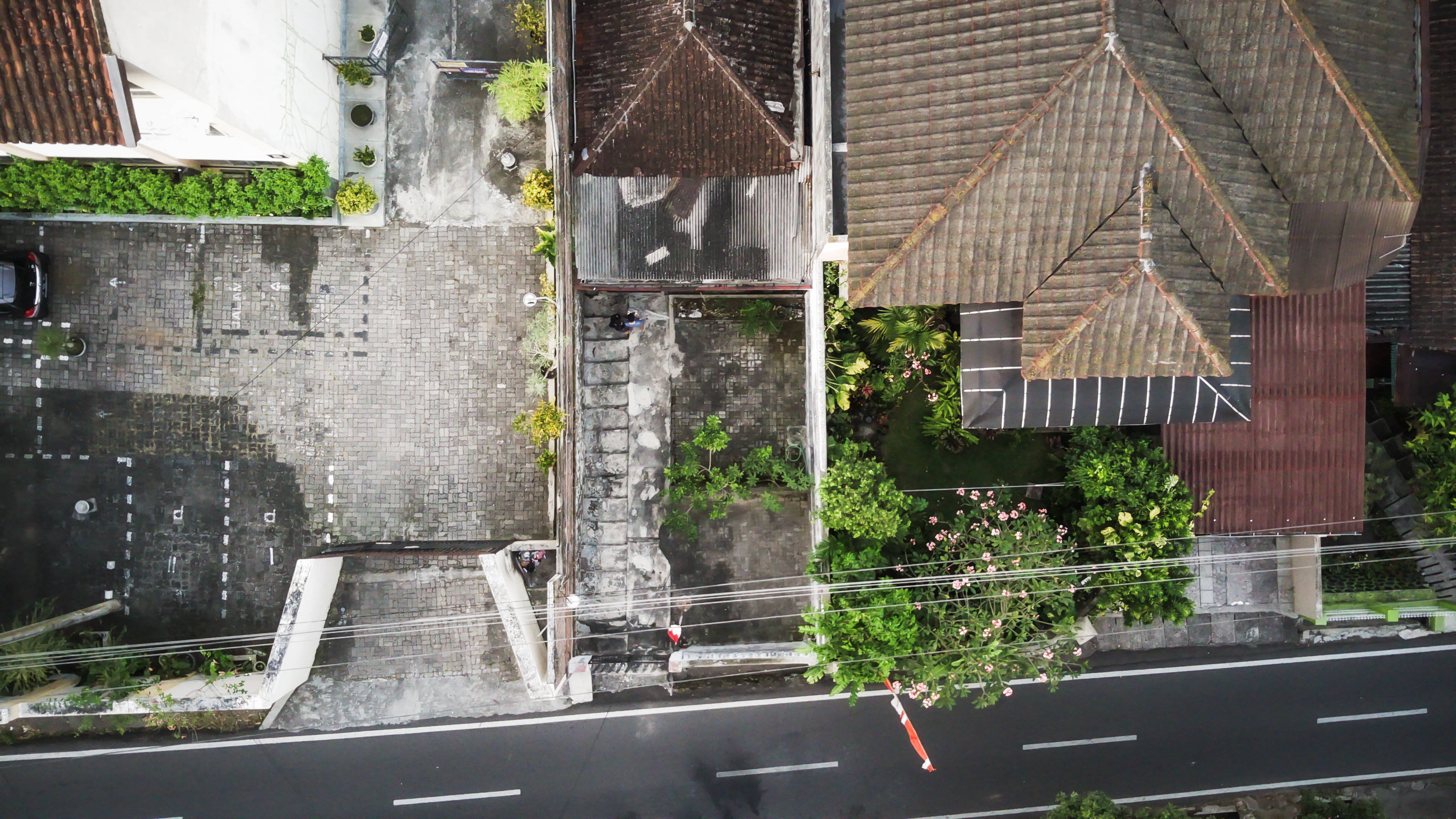 城市 桌布 壁紙 — 傳統瓦頂房屋坐落在鋪砌道路旁茂密綠植中的航拍視圖。