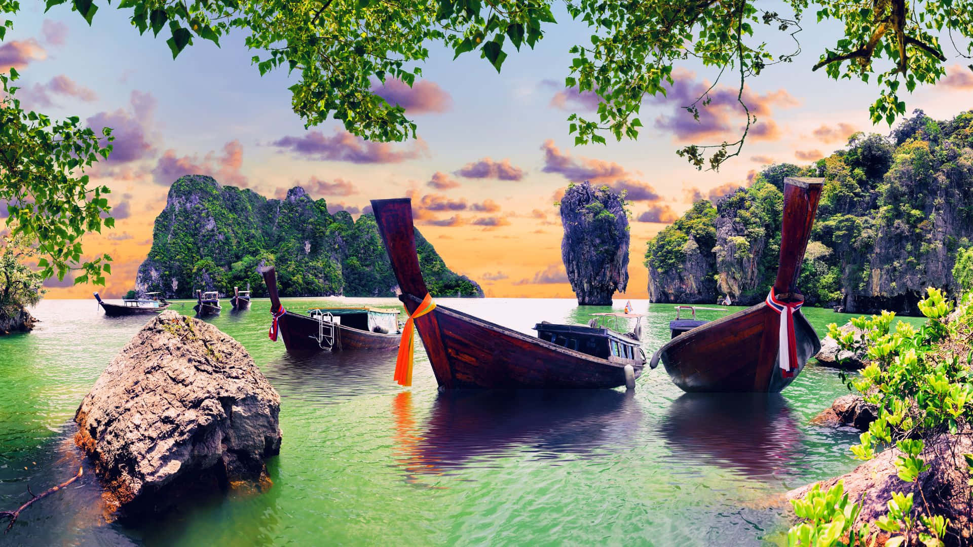 風景動畫 桌布 壁紙 — 傳統長尾船在日落時分停泊在翠綠的海水中，四周環繞著茂密的綠色植物和高聳的石灰岩懸崖。