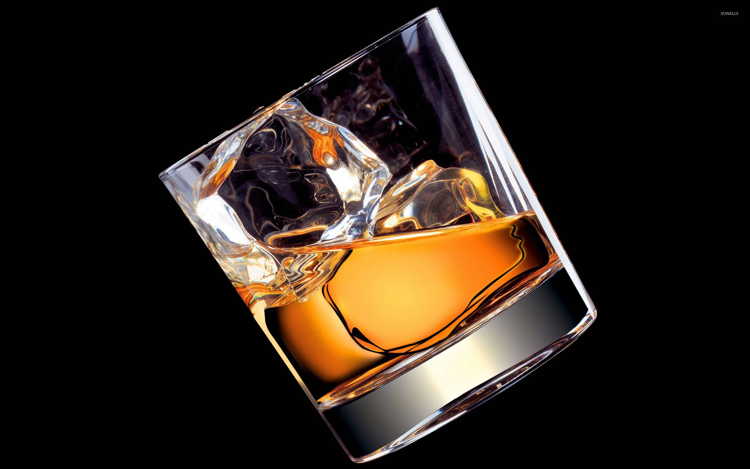 Drink 桌布 壁紙 — 傾斜的岩石杯裝滿琥珀色威士忌和大冰塊，在純黑背景上閃耀。