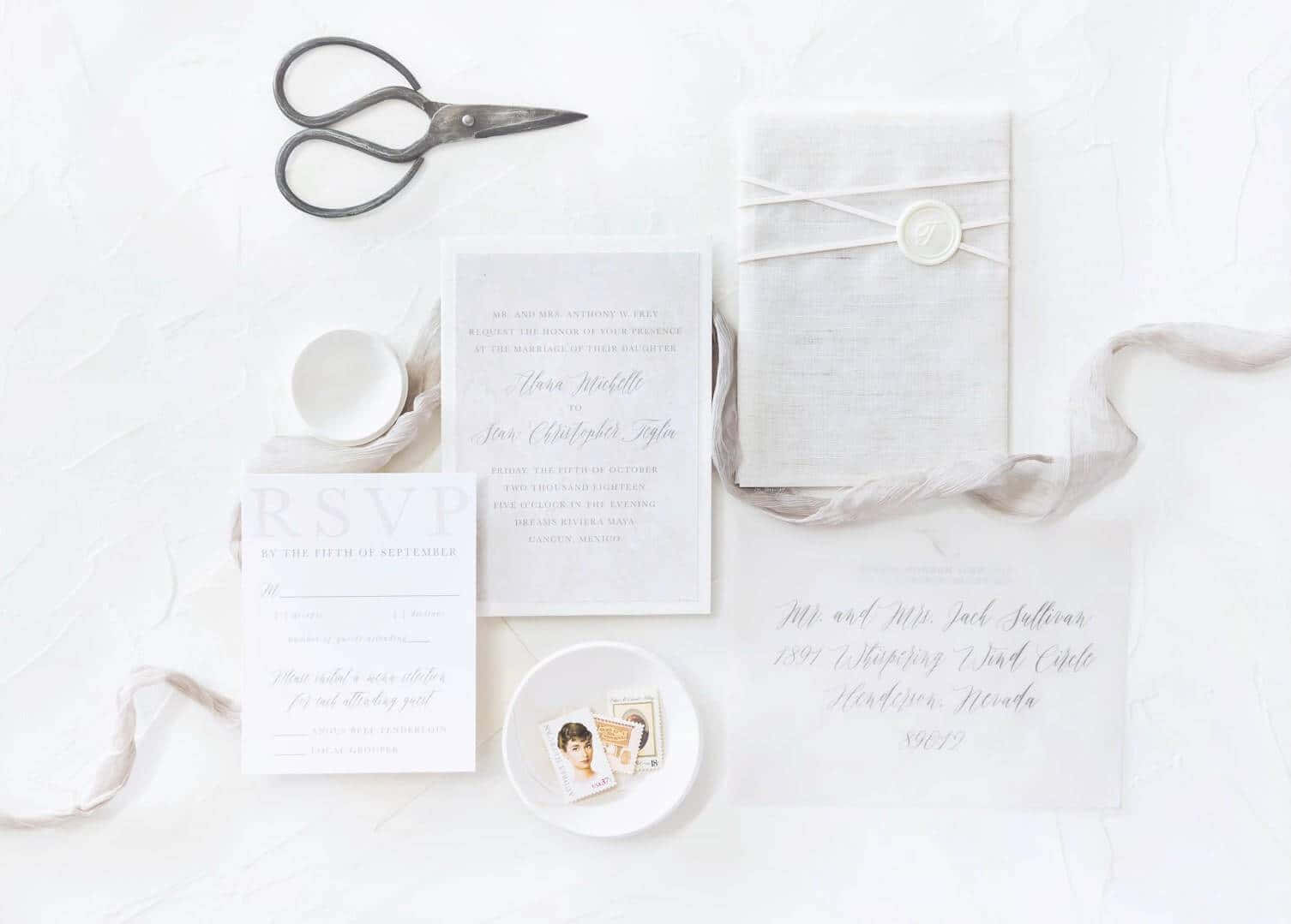 Flat Lay 桌布 壁紙 — 優雅婚禮邀請套裝，包括書法卡片、絲帶、火漆印章和復古剪刀，排列在紋理白色表面上。