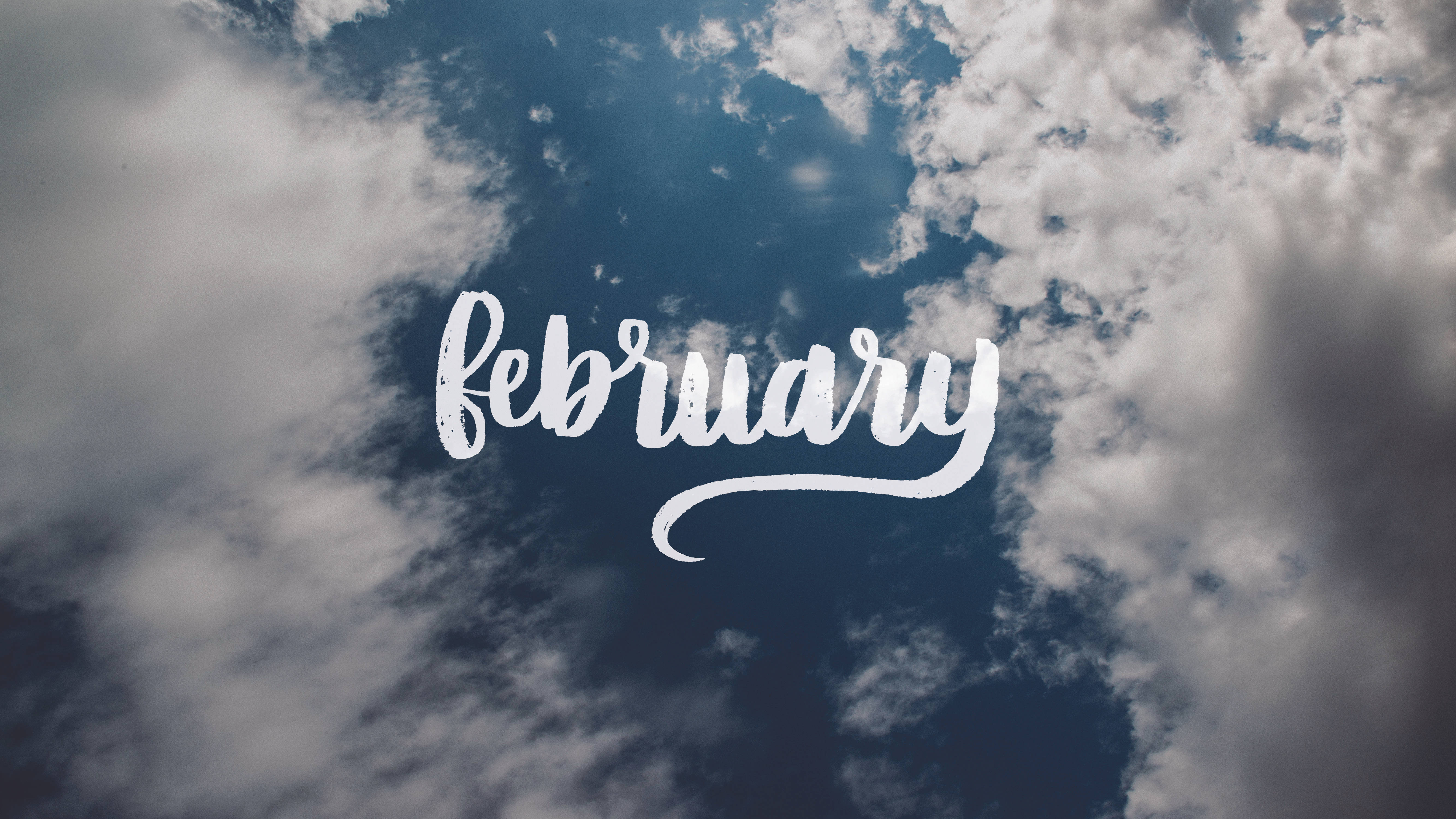 二月 桌布 壁紙 — 優雅白色字體的「february」一詞漂浮在點綴著蓬鬆白雲的動態藍天上。