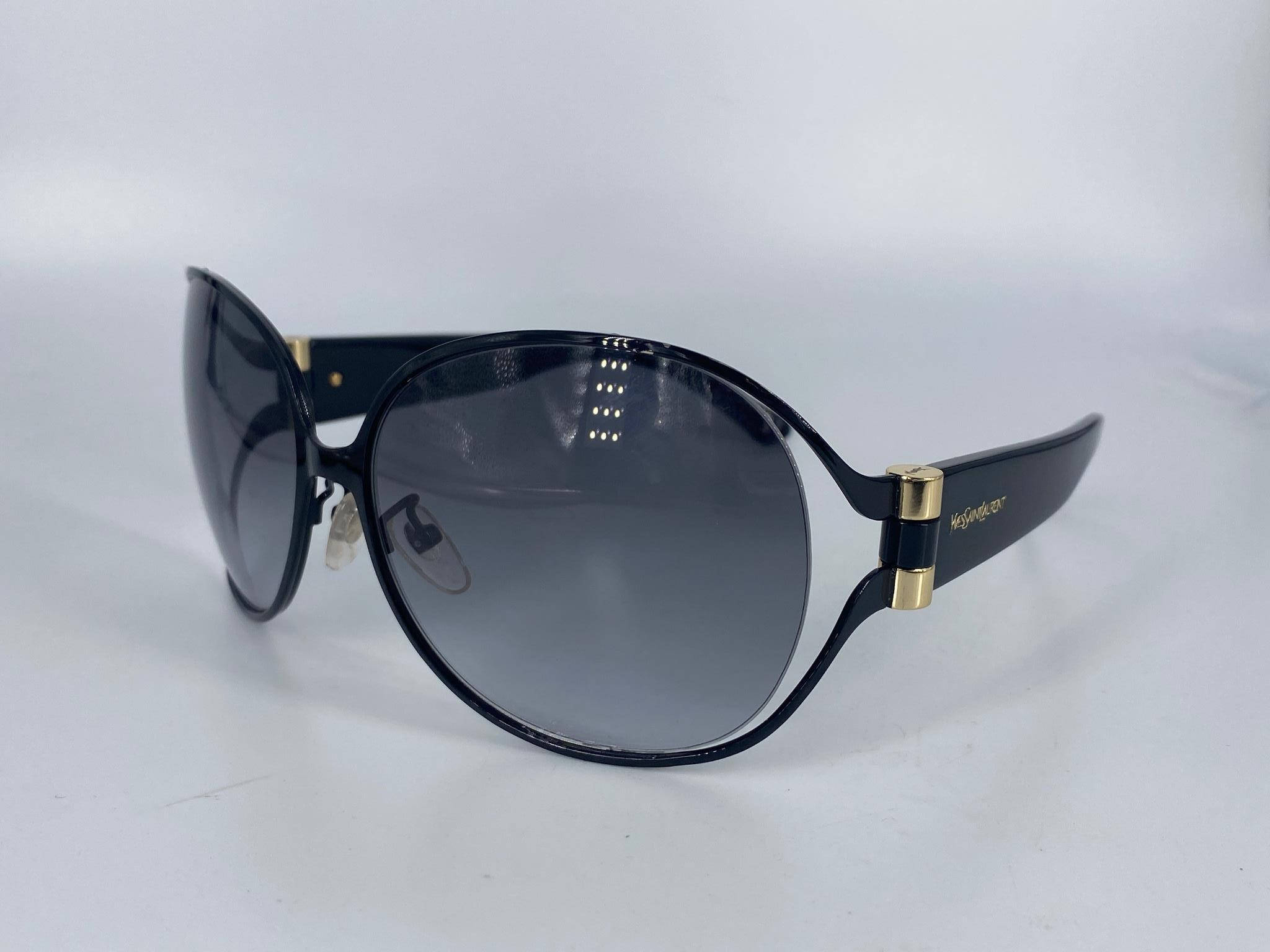 Ysl 桌布 壁紙 — 優雅的大尺寸黑色太陽眼鏡，帶有金色點綴和漸層鏡片，放置在純白色表面上。