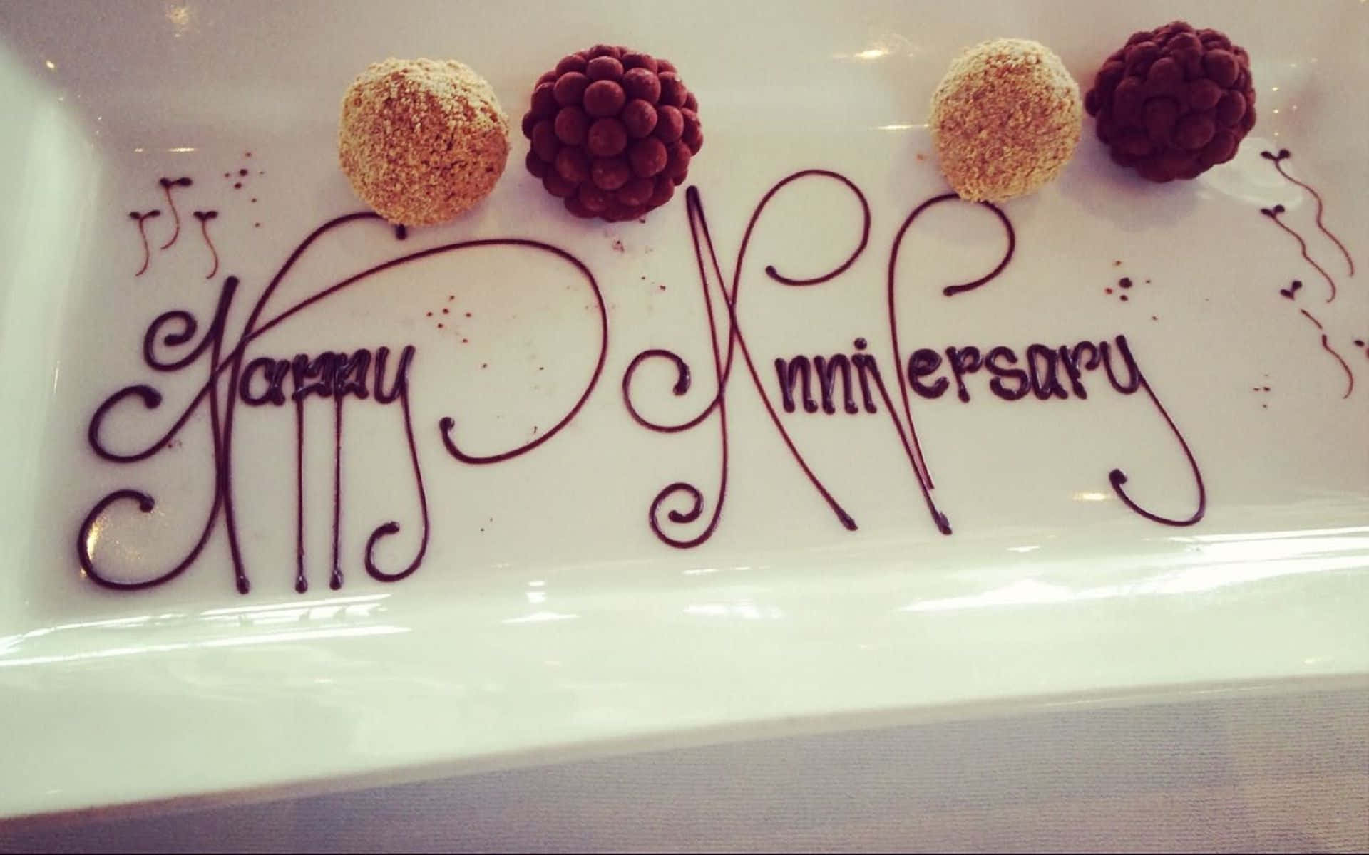 Chocolate 桌布 壁紙 — 優雅的巧克力字體在白色盤子上拼出「Happy Anniversary」，上方擺放四顆裝飾松露。